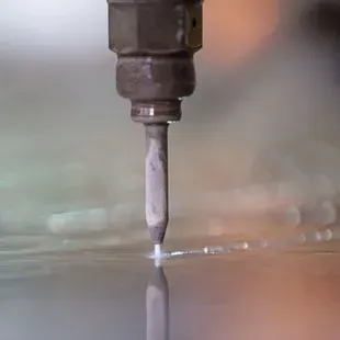 Une buse métallique émettant un jet d'eau à haute pression, découpant une tôle avec un effet brumeux.