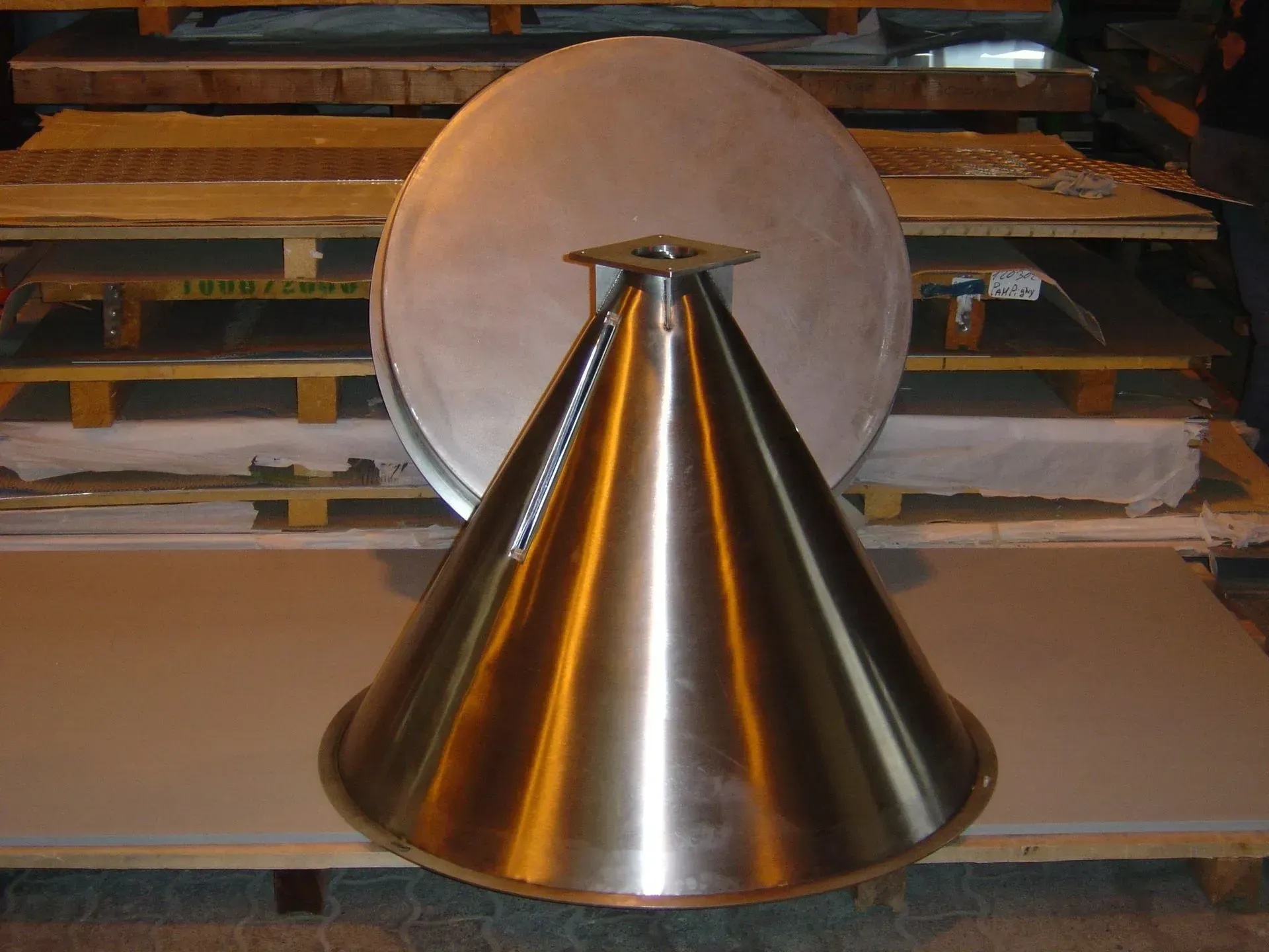 Antenne conique en acier inoxydable avec un réflecteur en forme de plat, posée sur une surface grise dans un entrepôt.