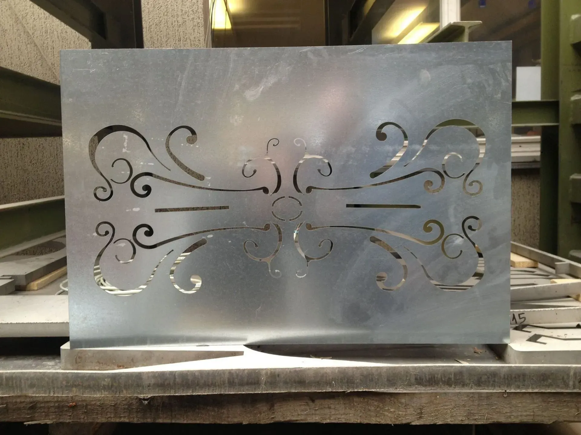 Tôle métallique avec un motif découpé orné, probablement pour une clôture ou un écran, dans un atelier.