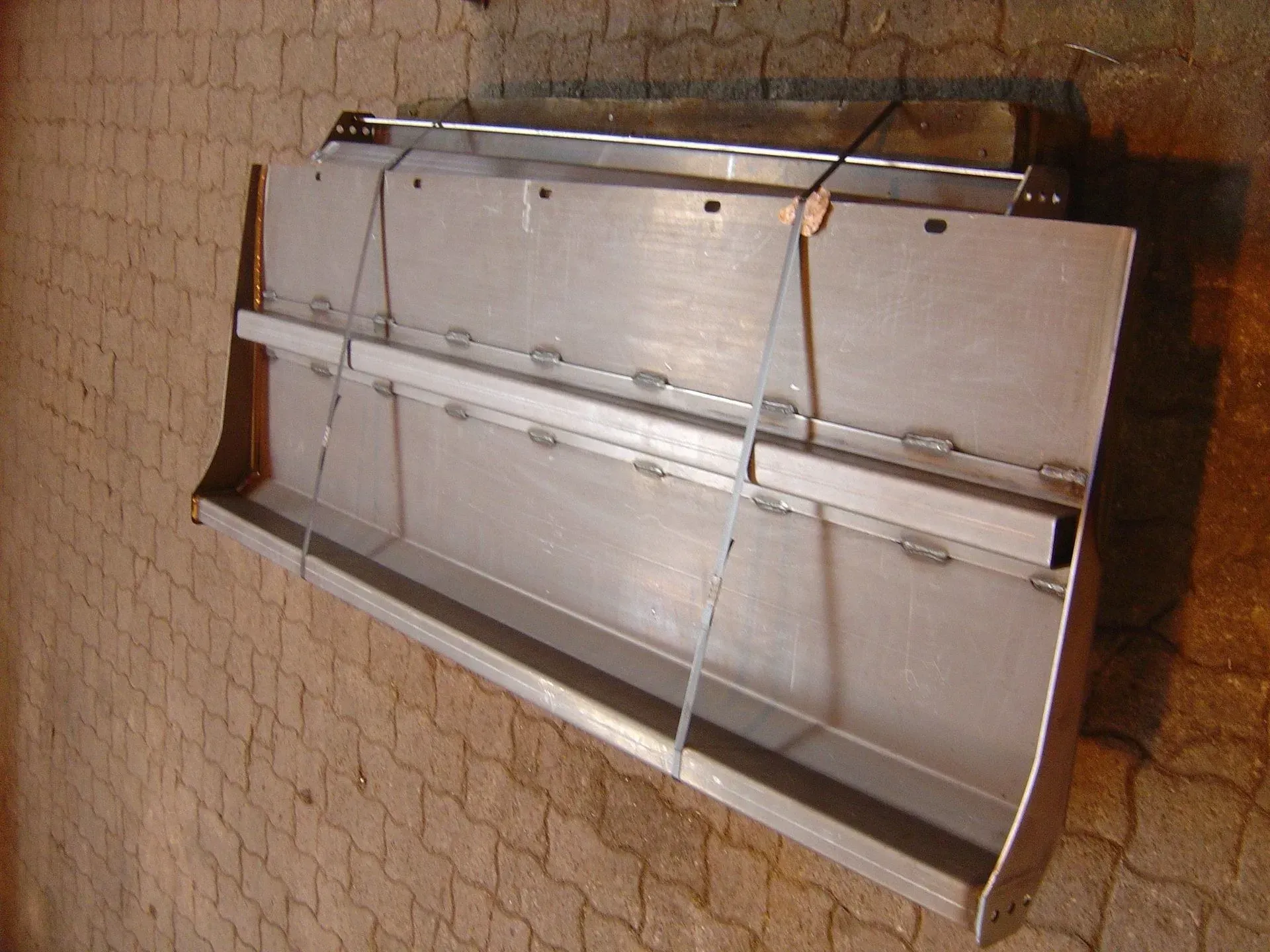 Lame de chasse-neige en métal reposant sur une surface en brique; fixée par un câble.