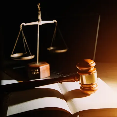 El mazo de un juez está colocado encima de un libro abierto delante de una balanza de justicia.
