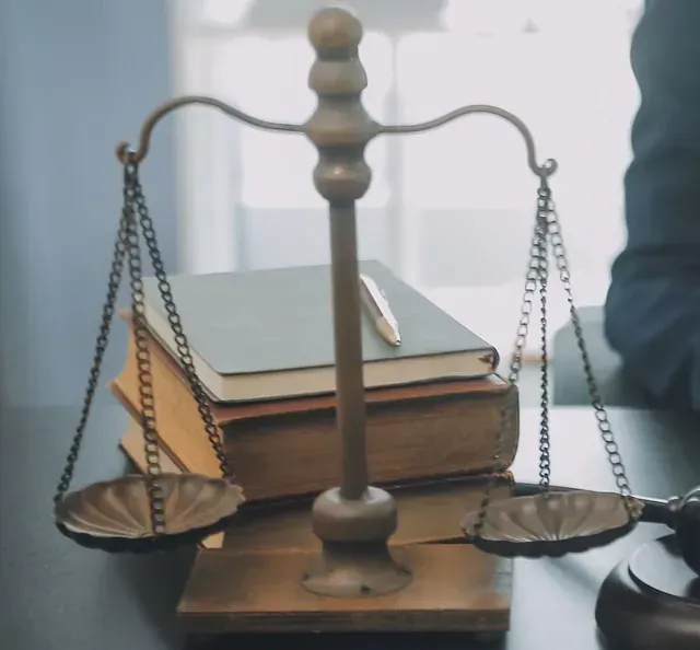 Una balanza de la justicia reposa sobre una mesa junto a libros y un bolígrafo.