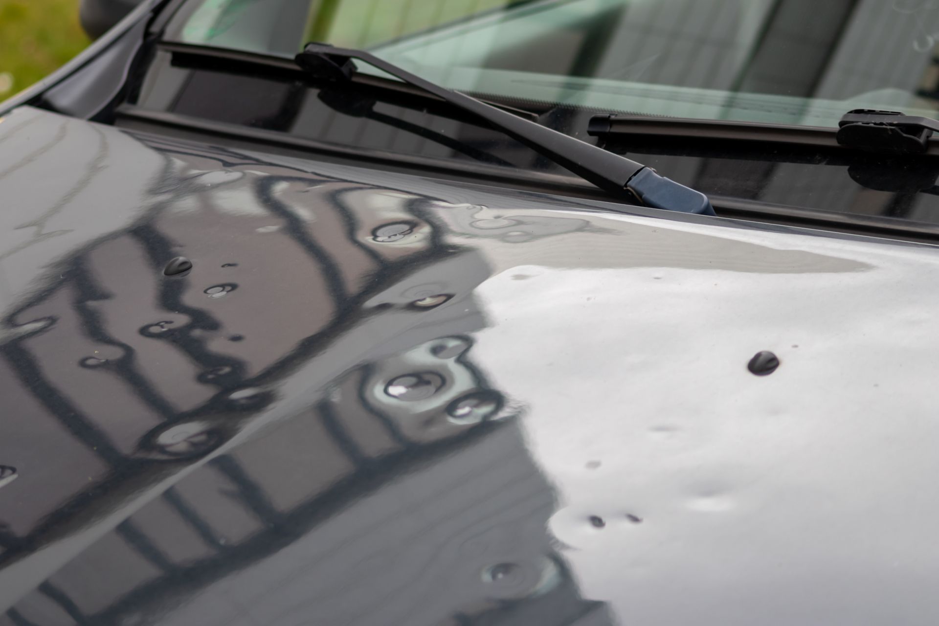 Capot de voiture avec impact de grêle, reflet d'un bâtiment sombre et essuie-glaces visibles