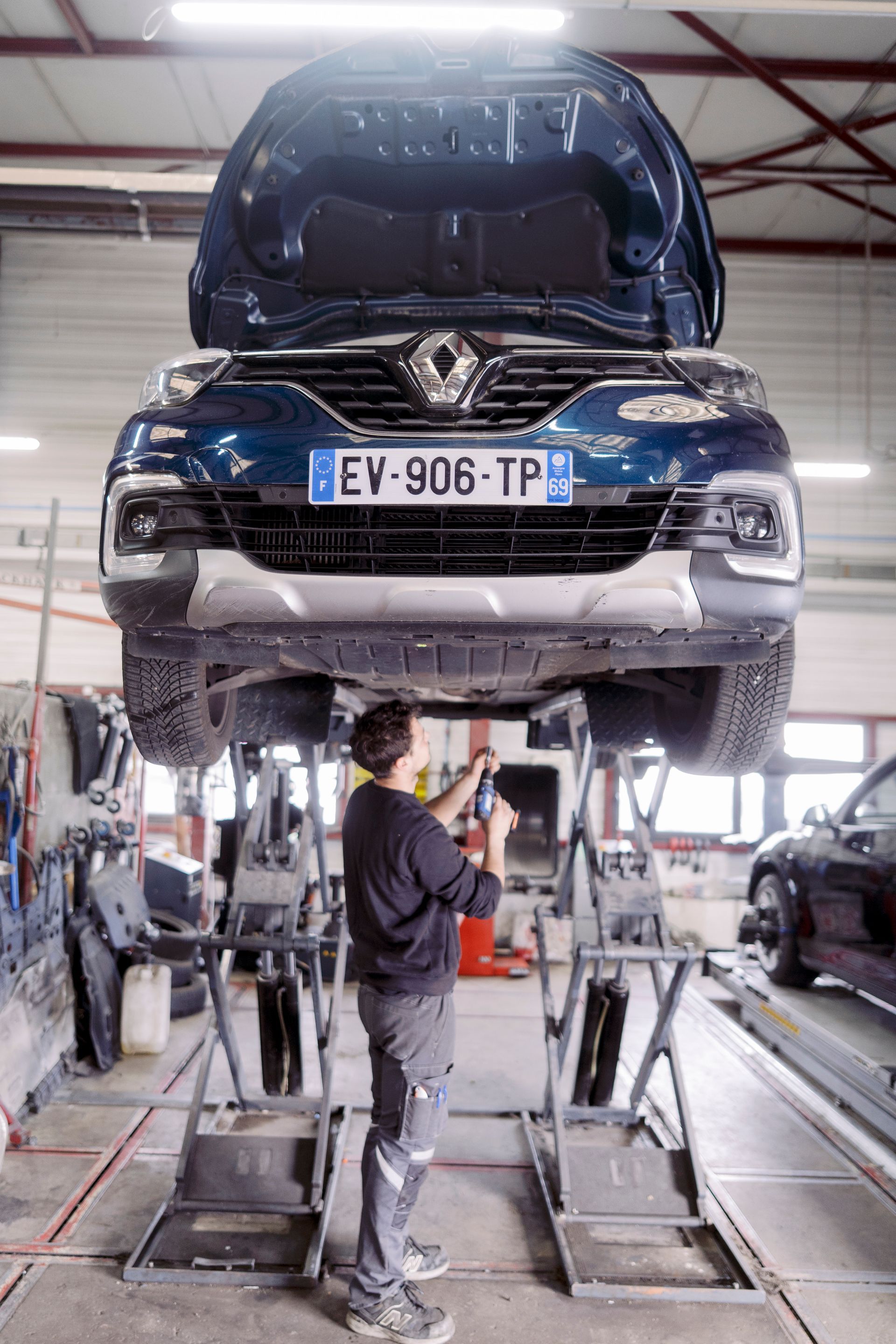 Une voiture bleue est soulevée sur un pont élévateur dans un garage, un mécanicien travaille dessous.