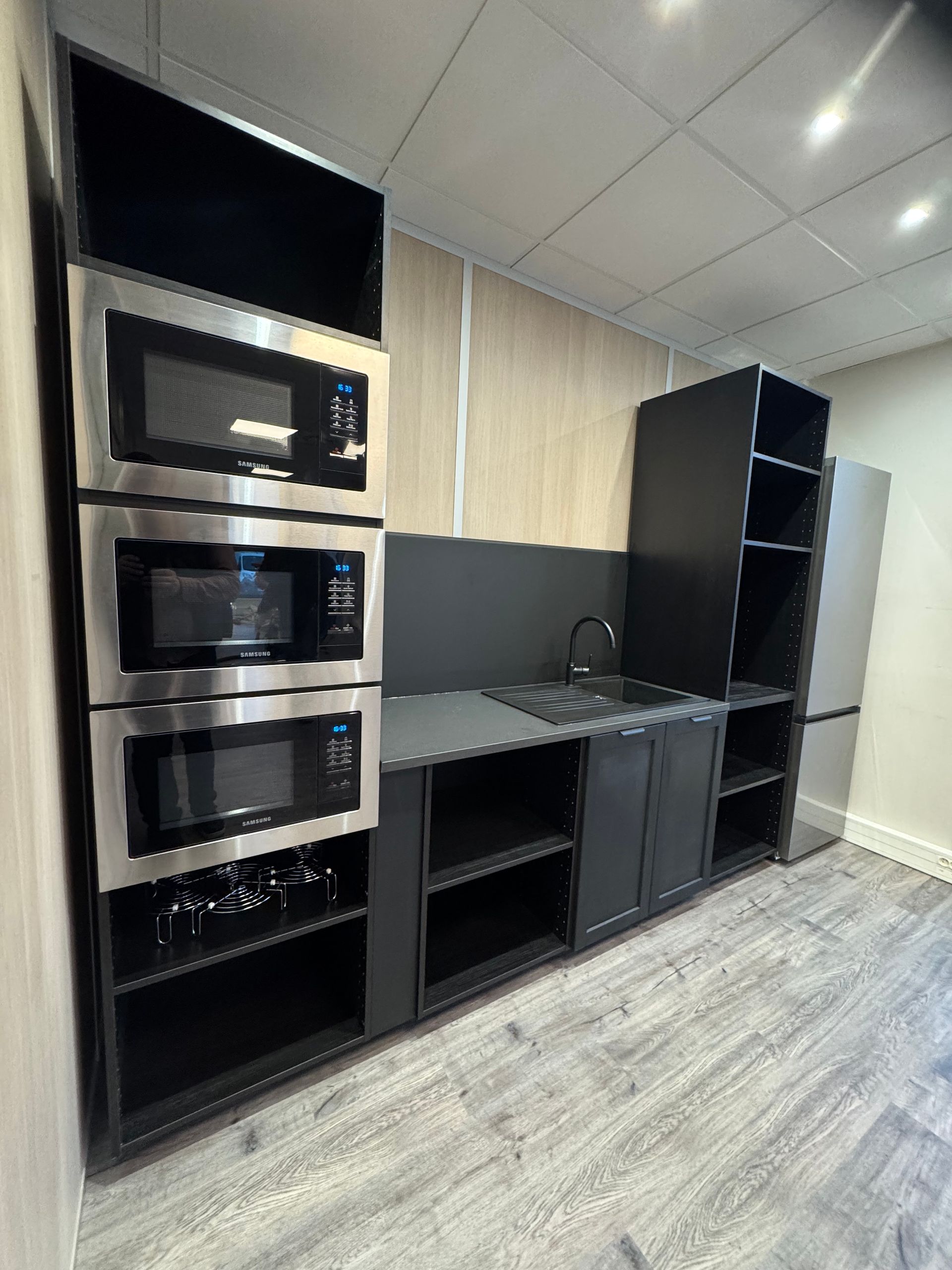 Petite cuisine avec micro-ondes en acier inoxydable, placards noirs et évier.