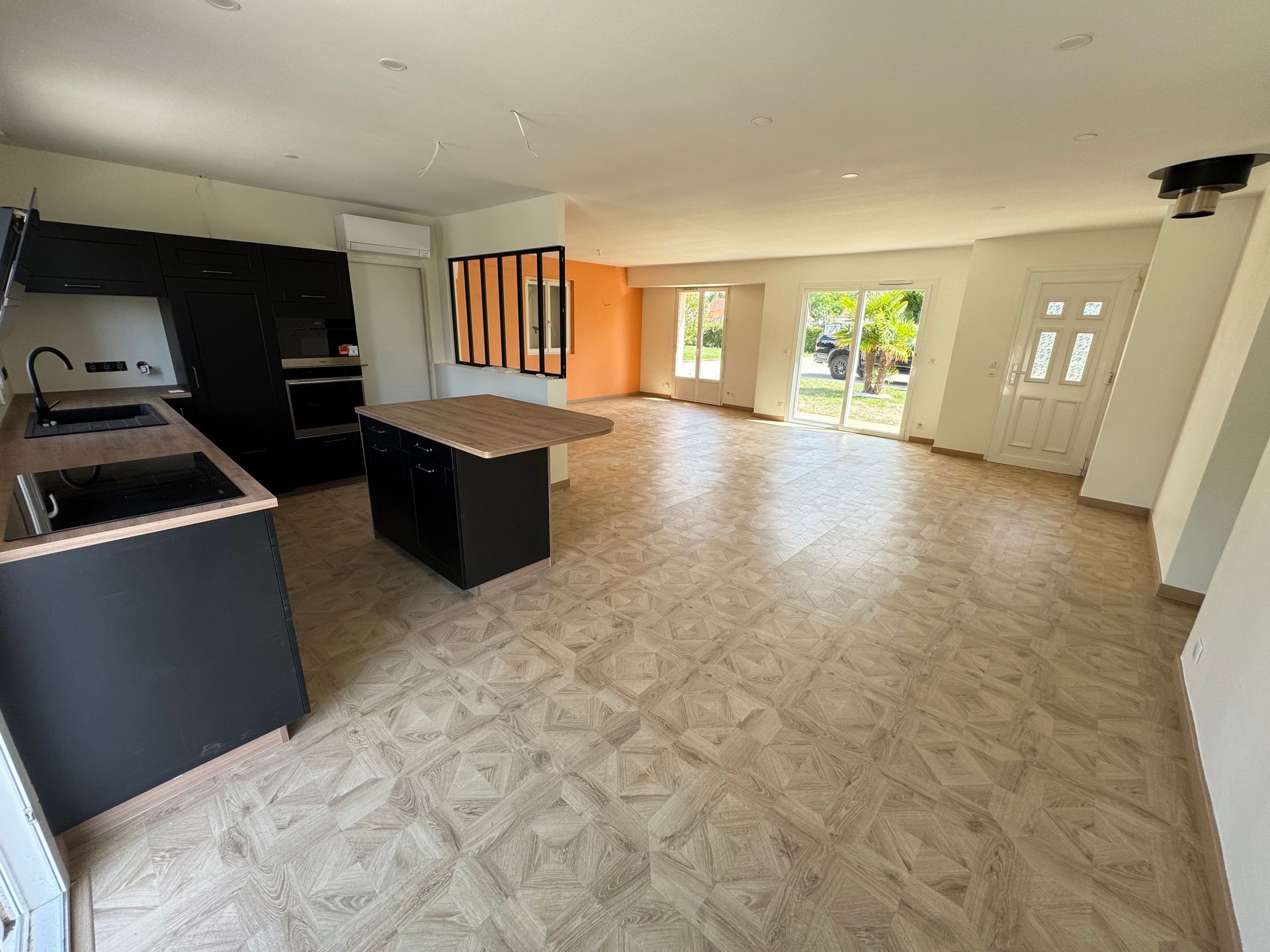 Cuisine et séjour avec armoires noires, îlot et grandes portes vitrées.