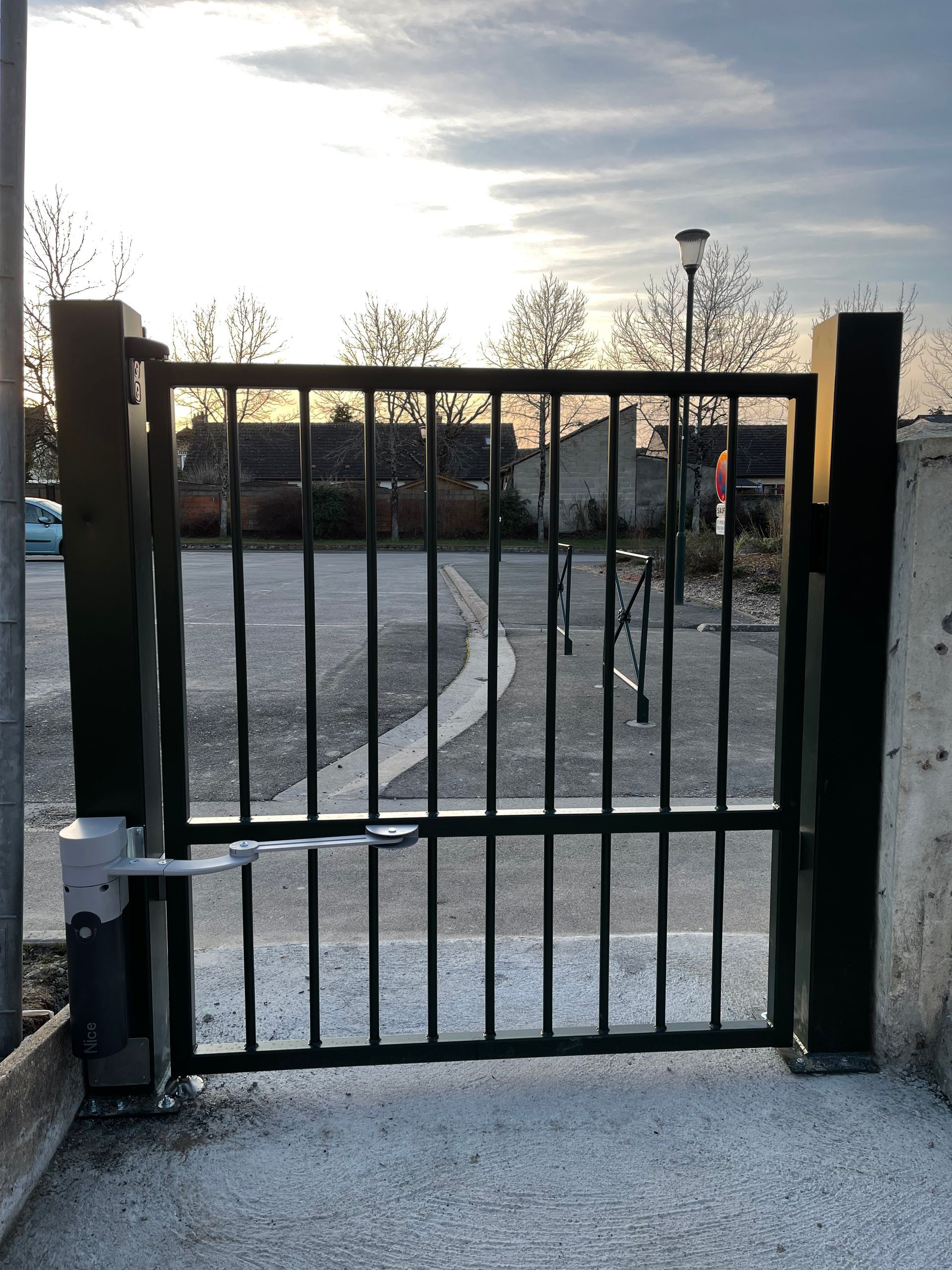 Portail métallique noir dans un parking, fixé à un bras motorisé.