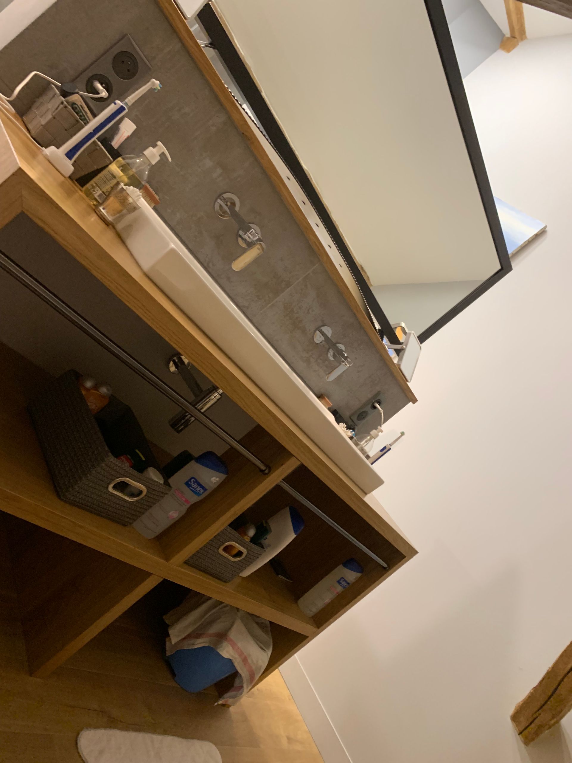Meuble-lavabo de salle de bain avec étagères en bois, miroir et articles de toilette.