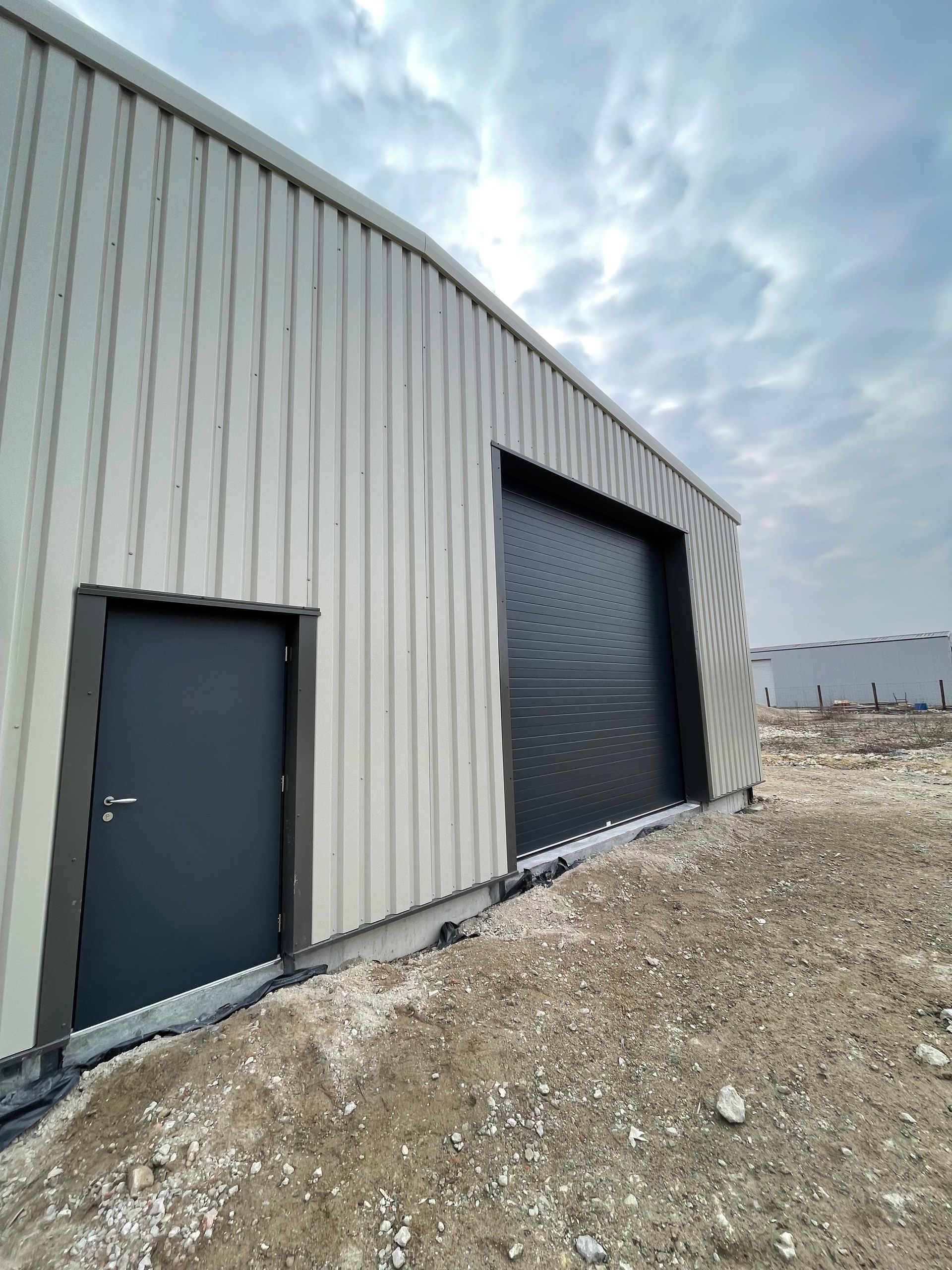 Extérieur d'un bâtiment commercial avec une porte noire et une grande porte roulante, posé sur du gravier.