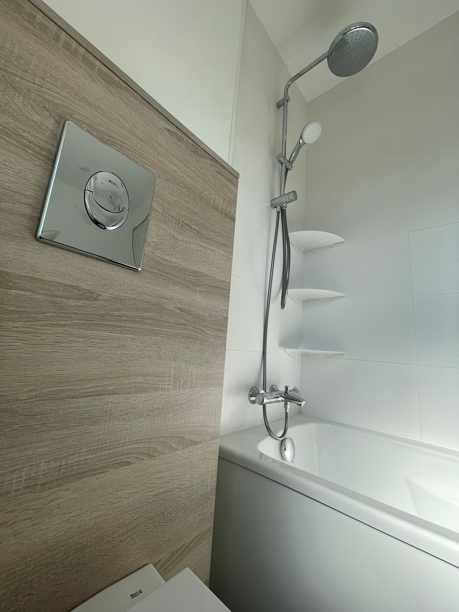 Salle de bains avec baignoire, pommeau de douche, étagères et mur texturé.