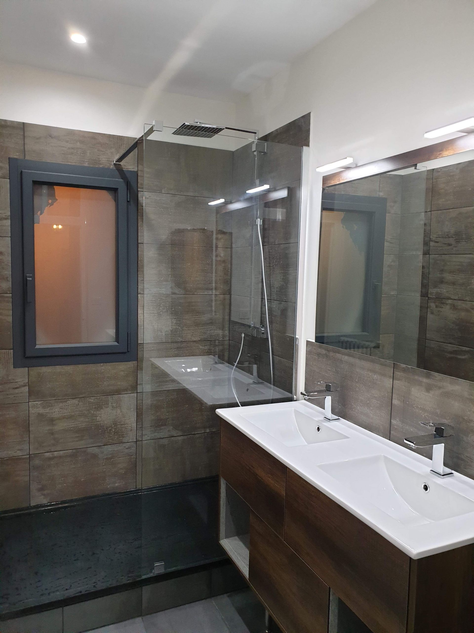 Salle de bains moderne avec meuble-lavabo en bois, double vasque, grand miroir et douche carrelée de gris foncé.