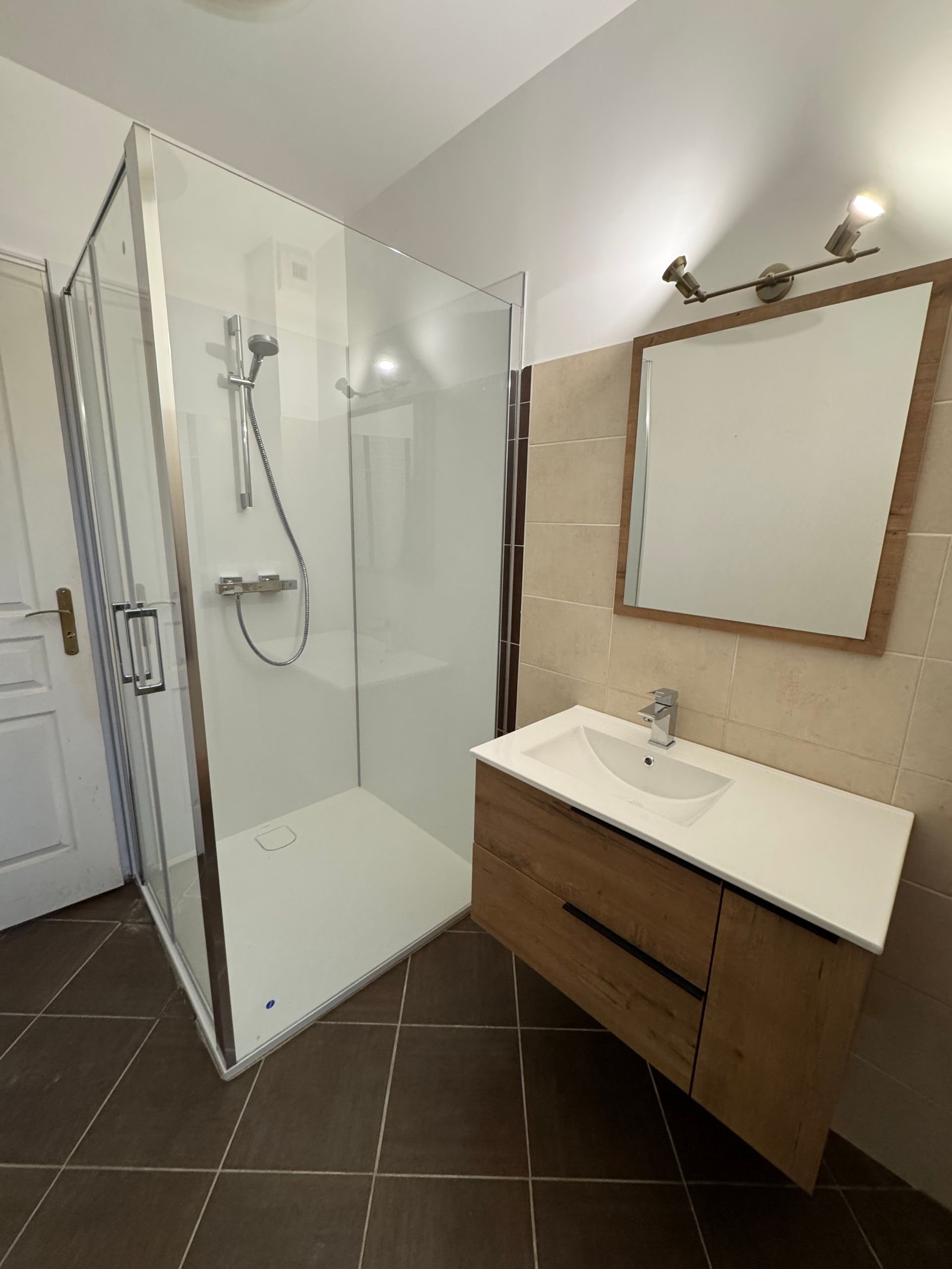 Cabine de douche avec murs carrelés gris foncé et portes en verre. Robinetterie argentée et receveur de douche blanc.