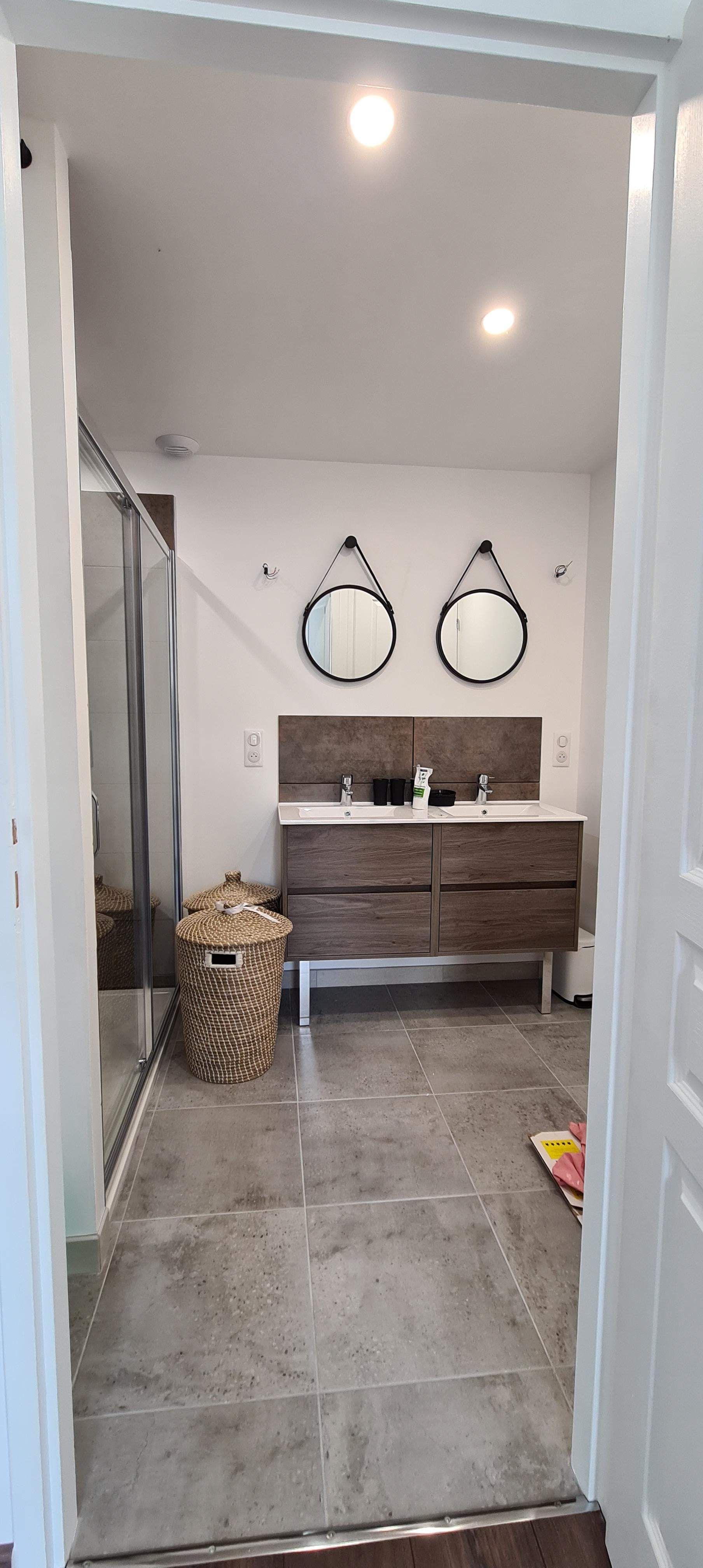 Salle de bains avec double vasque, deux miroirs ronds et un panier tressé.