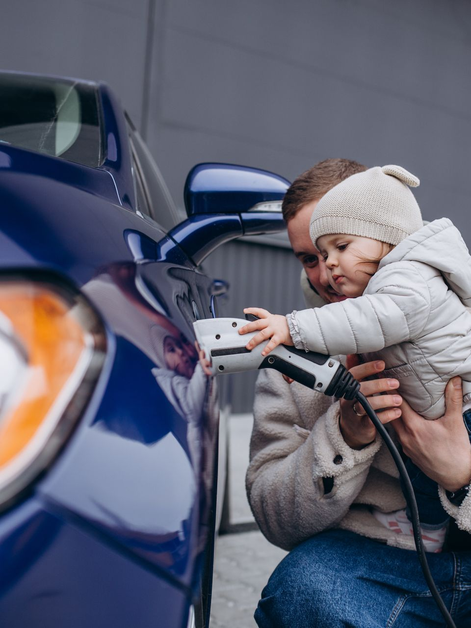 Un homme et un enfant chargent une voiture électrique bleue.