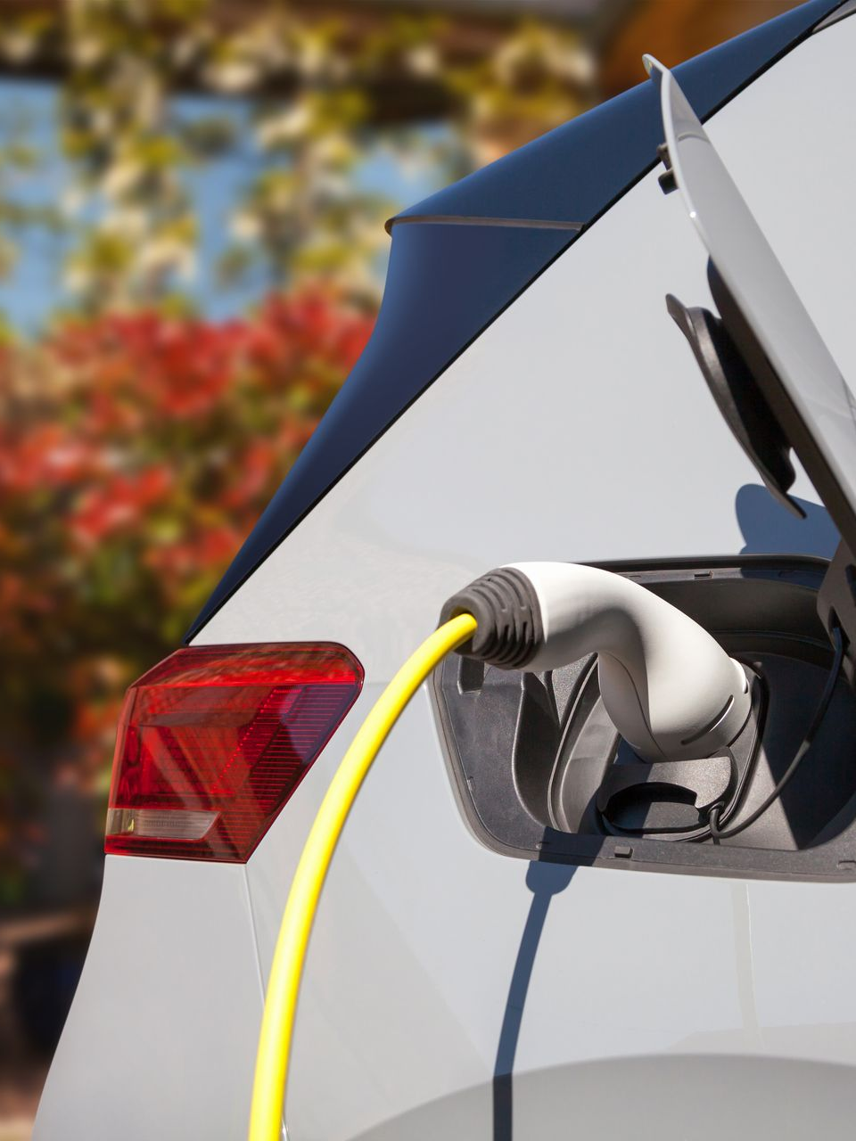 Voiture électrique blanche en charge à l'extérieur avec un câble de charge jaune.