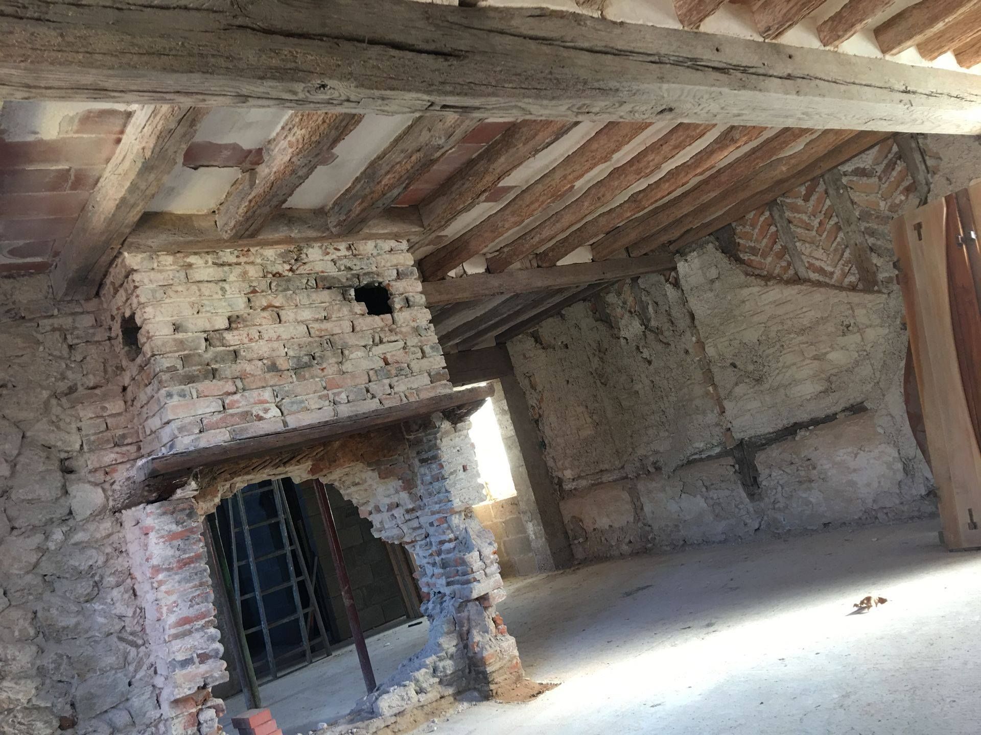 Intérieur d'un bâtiment rustique avec poutres apparentes, cheminée en briques et murs en pierre.