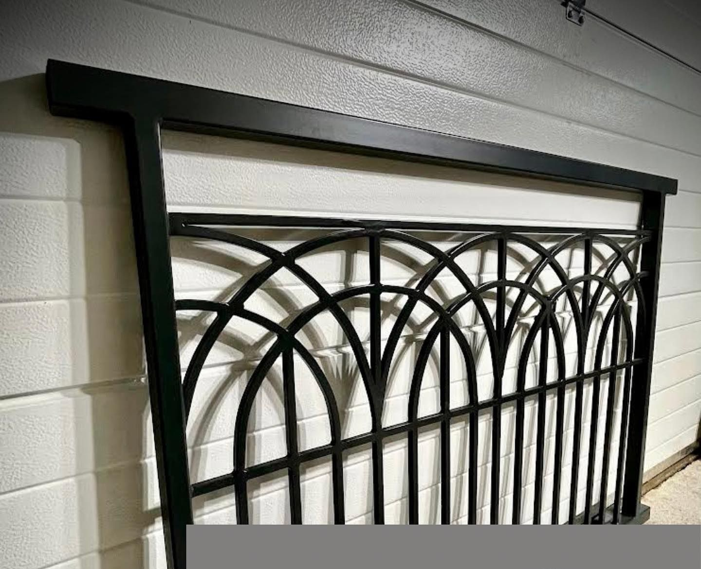 Portillon en fer forgé noir contre un mur blanc.