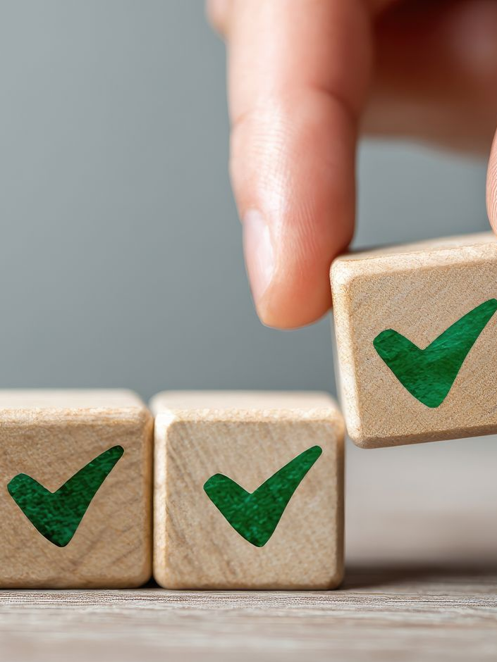 Main plaçant un cube en bois avec une coche verte à côté de deux autres sur une surface.