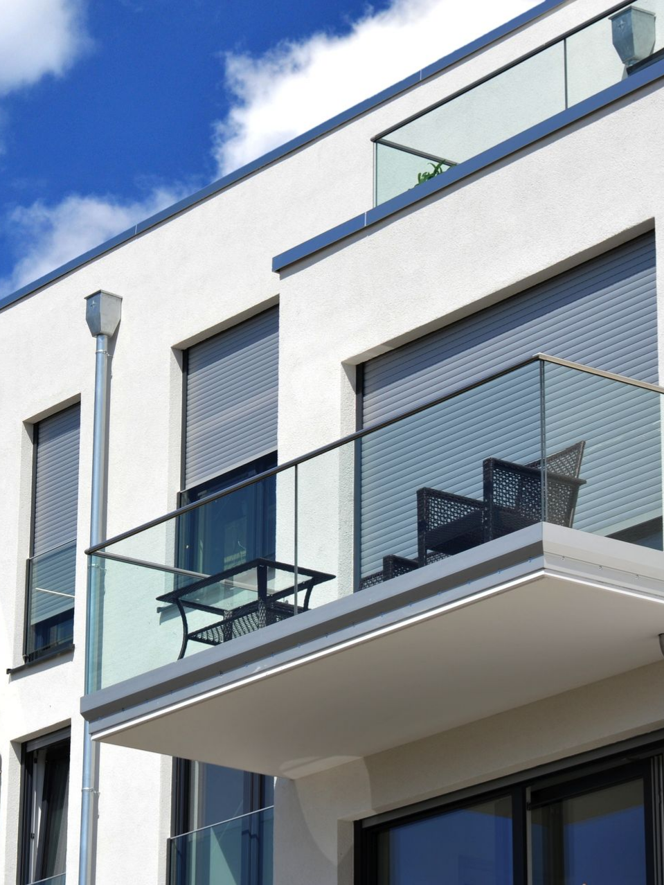 Immeuble d'appartements blanc moderne avec balcons en verre, ciel bleu en arrière-plan.