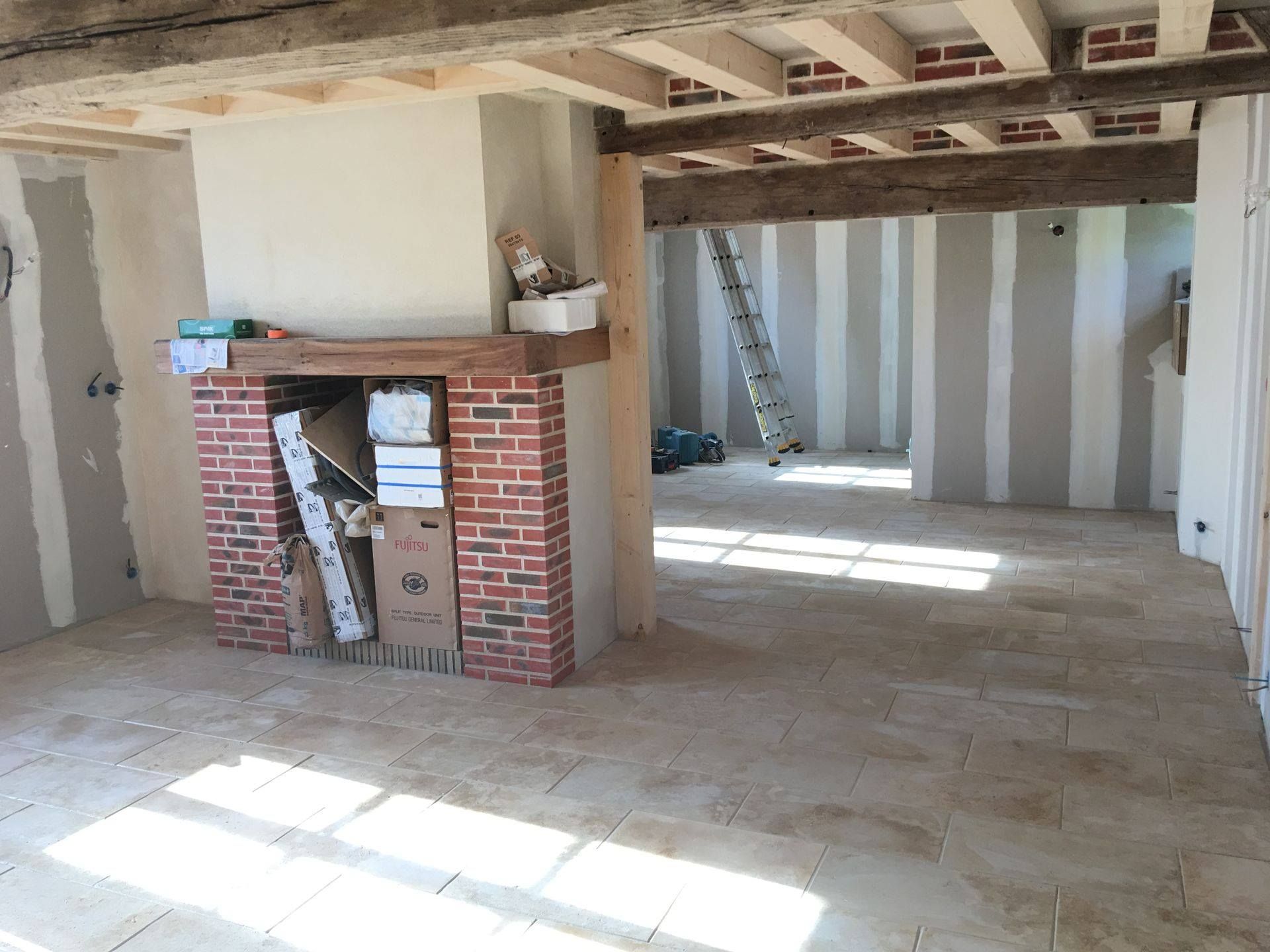 Intérieur rénové : cheminée en brique, poutres apparentes, mur rayé, matériaux de construction et lumière naturelle.