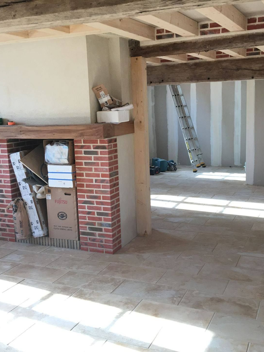 Salon en cours de rénovation avec poutres apparentes, cheminée en brique et sol en pierre.
