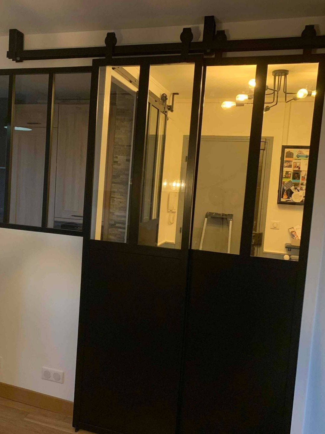 Portes coulissantes en verre à cadre noir et portes pleines sur rail, reflétant une pièce avec des lumières et de la décoration.