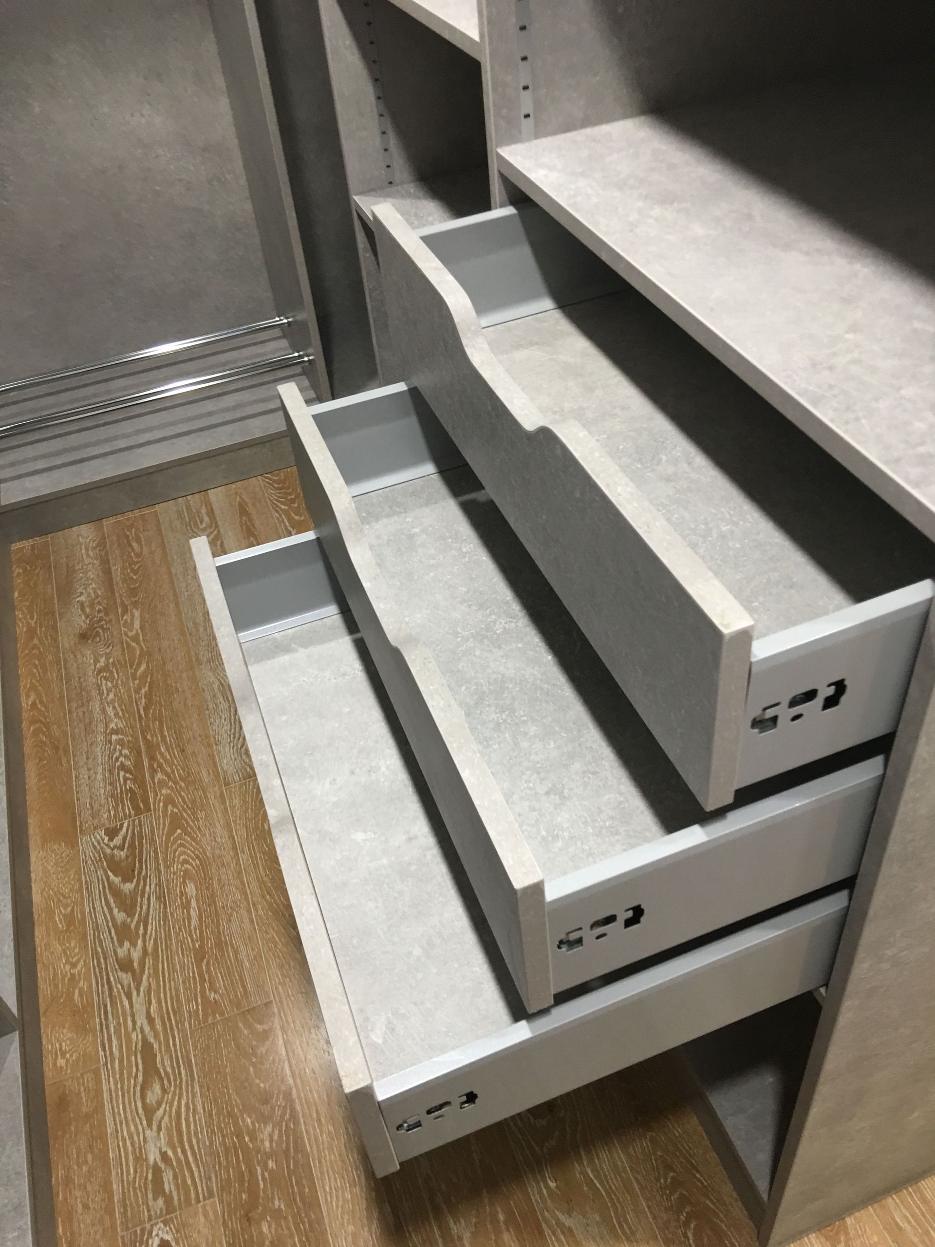 Trois tiroirs gris ouverts dans un placard avec parquet et étagères grises.