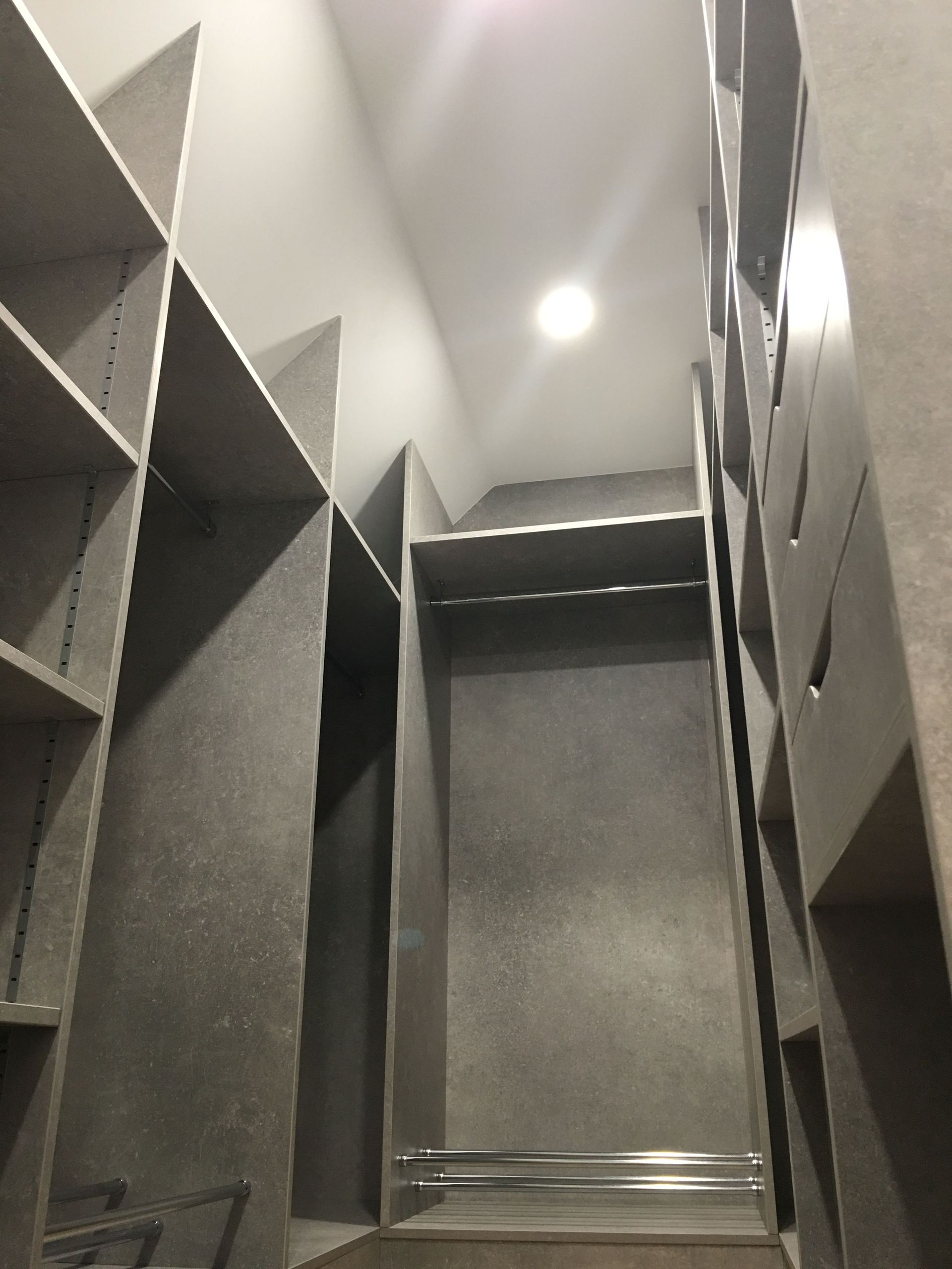 Dressing gris vide avec étagères et tringle à vêtements, sous un éclairage vif au plafond.
