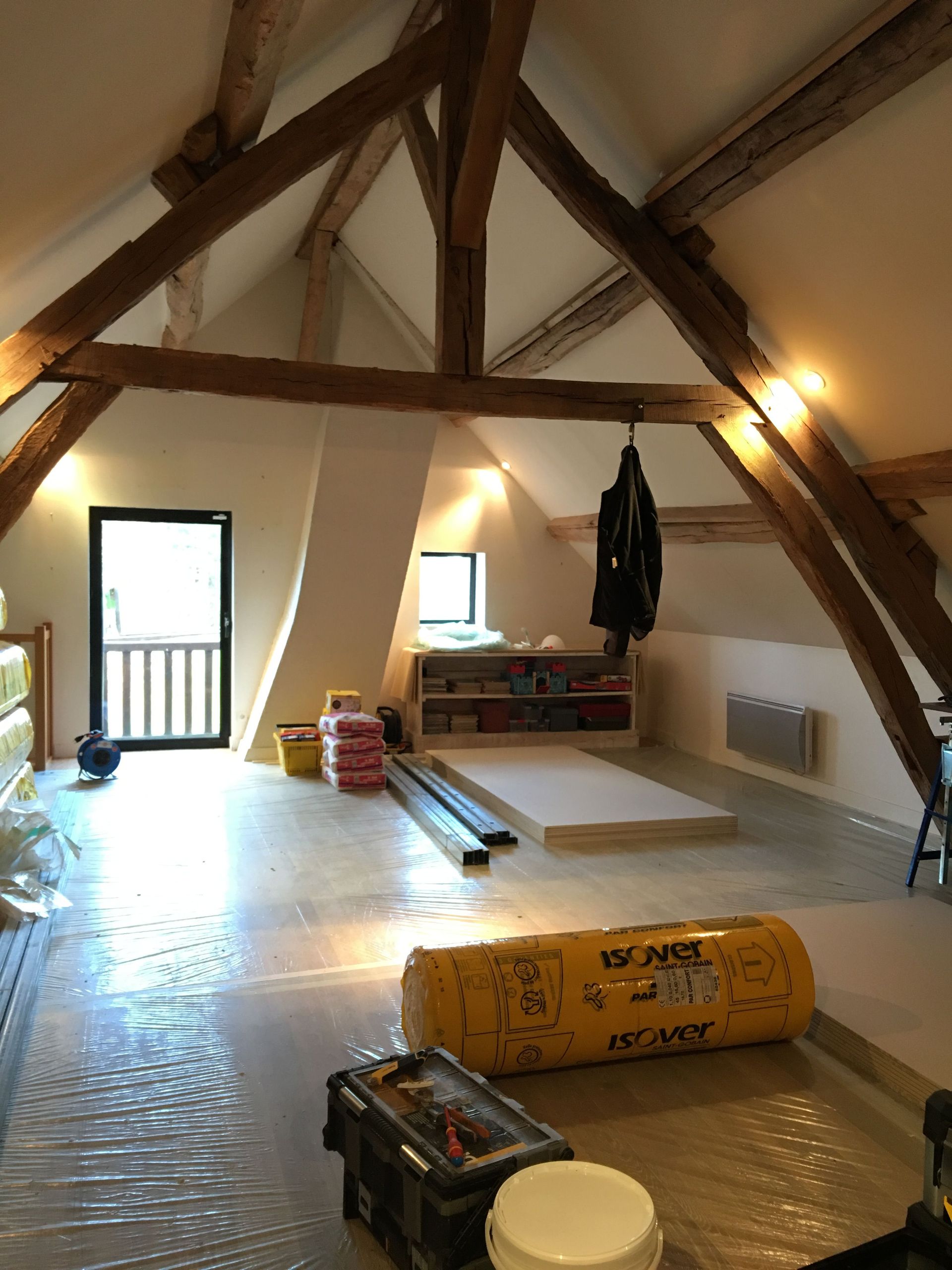 Intérieur d'un grenier avec poutres en bois apparentes, une porte et des matériaux de construction au sol.