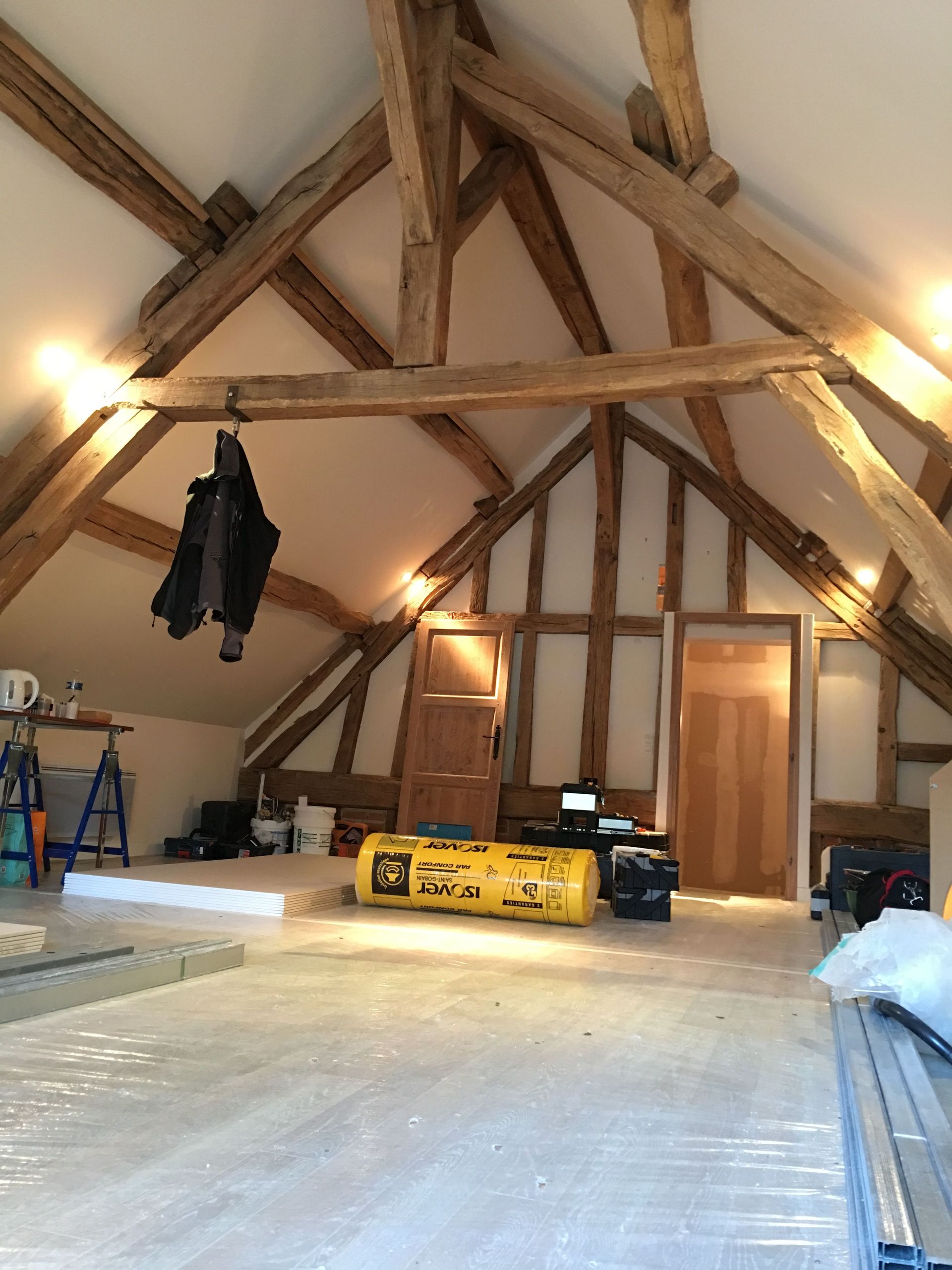 Grenier spacieux en cours de rénovation, poutres apparentes, sol non fini, matériel de chantier, porte.