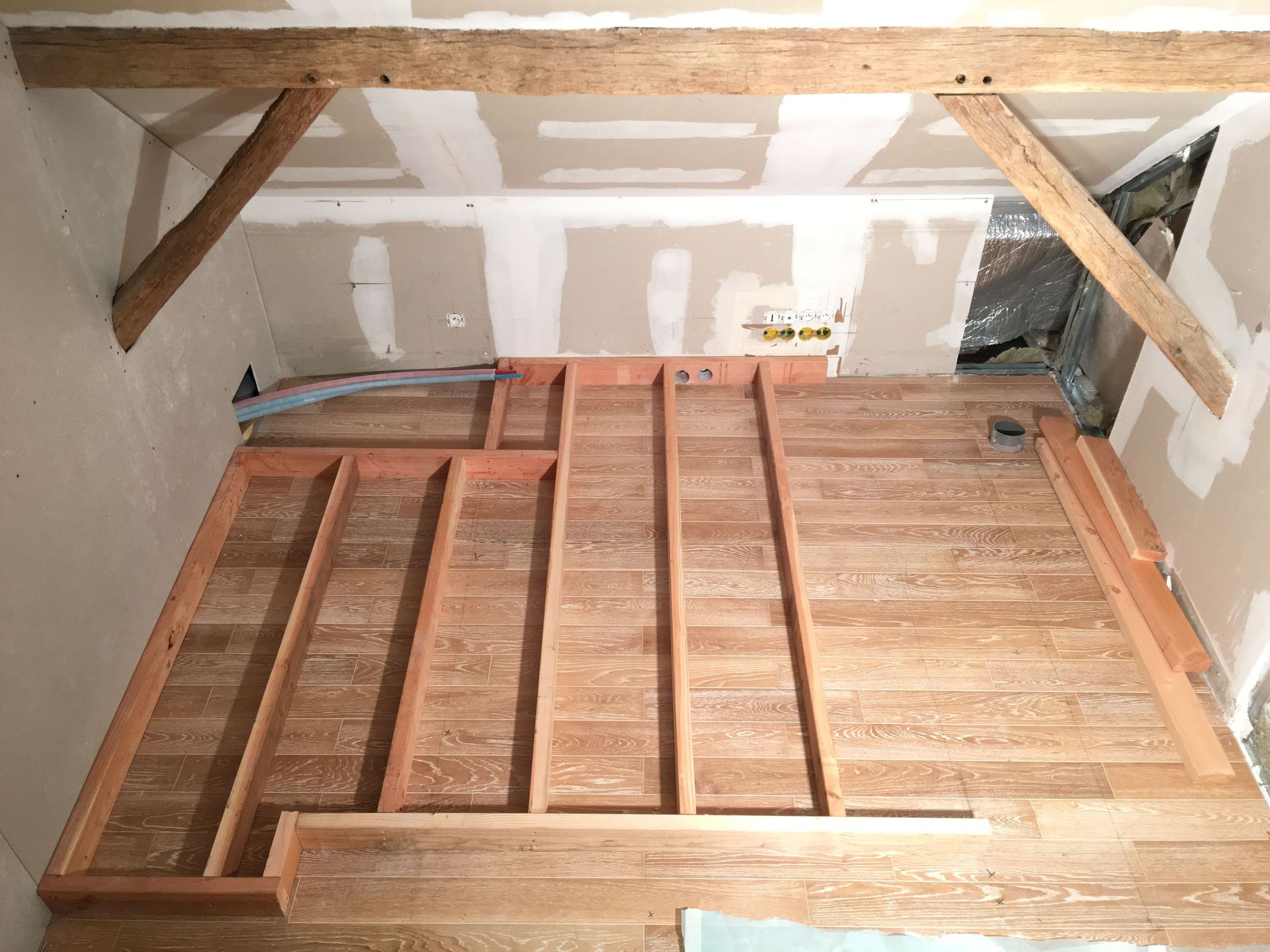 Construction d'un plancher en bois dans une pièce, avec poutres apparentes et murs en plaques de plâtre.