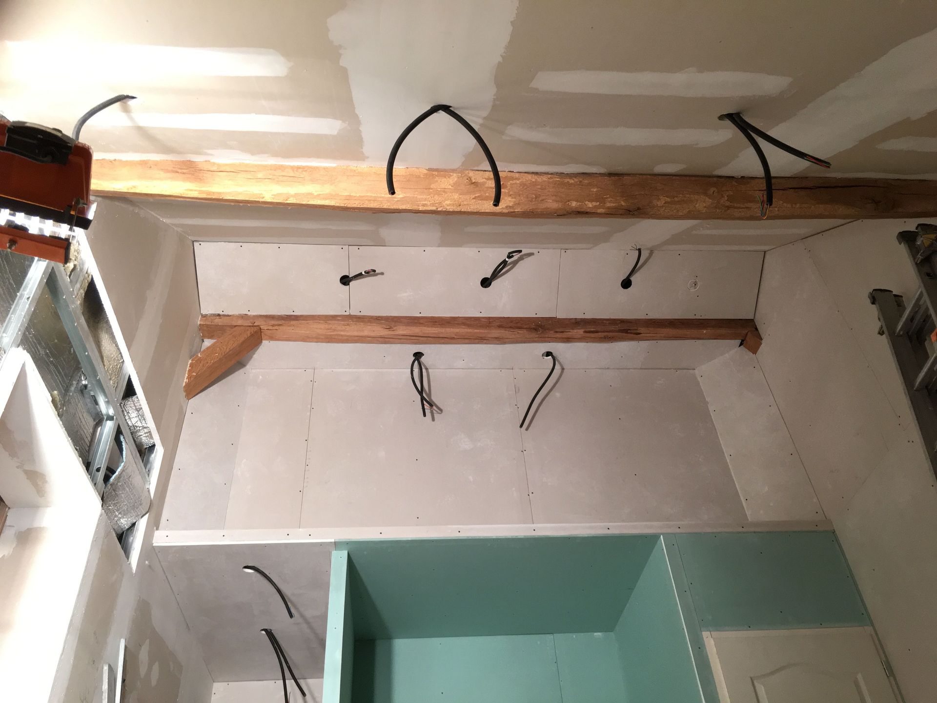 Aménagement intérieur avec câblage apparent, poutres en bois, cloisons sèches et meubles partiellement construits.