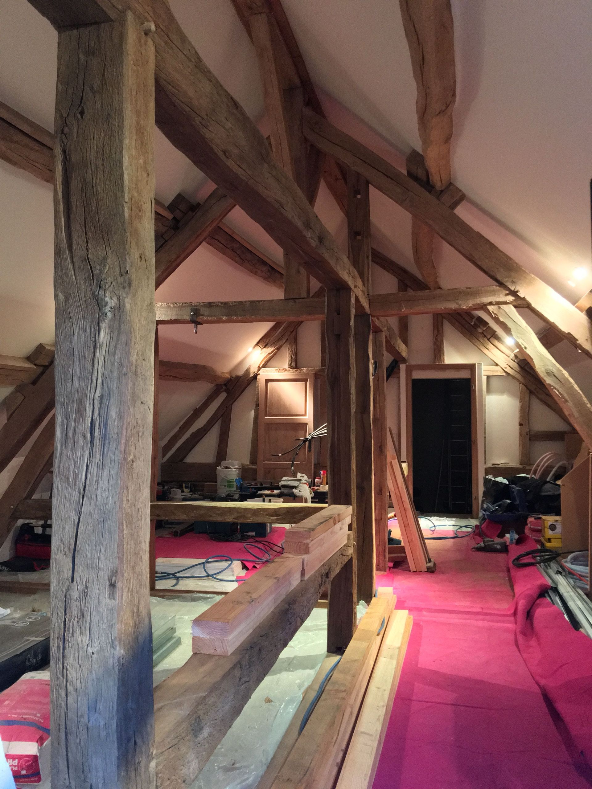 Grenier rénové avec poutres apparentes, revêtement de sol rose et outils de construction.