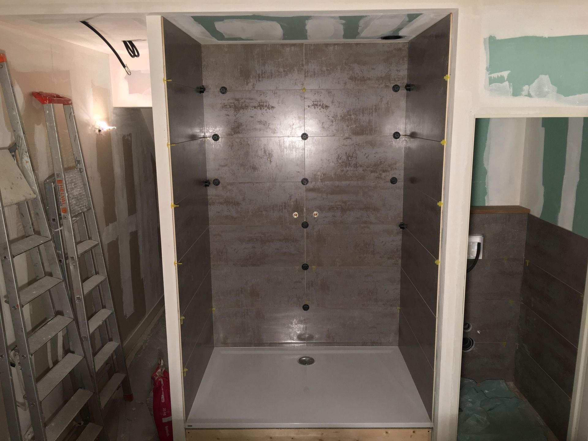 Cabine de douche en construction, avec murs et receveur carrelés. On aperçoit les plaques de plâtre et des outils comme des échelles.