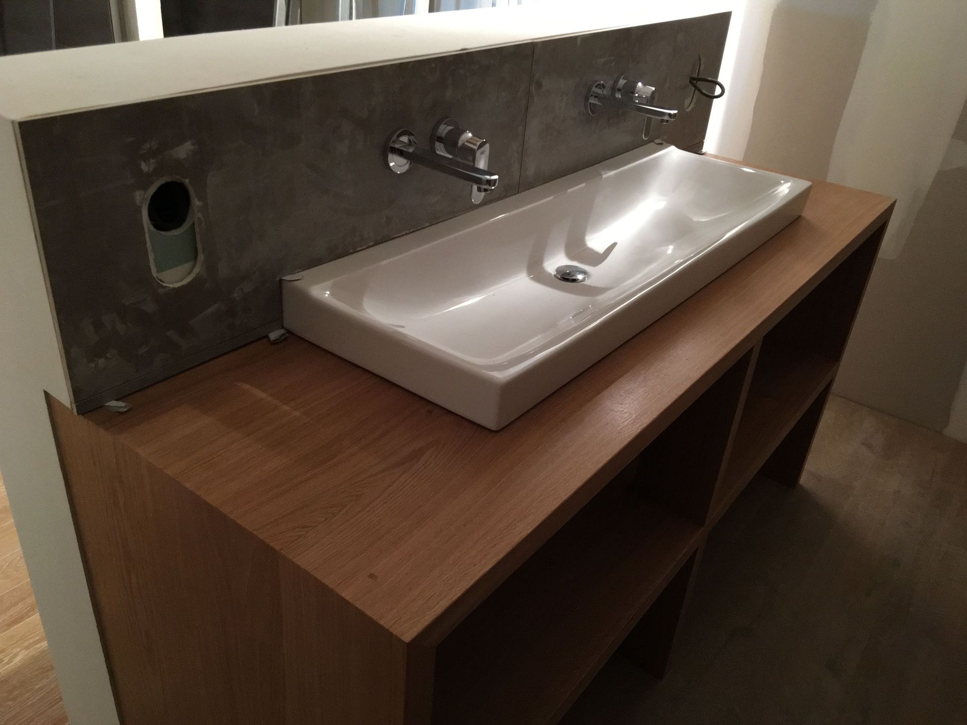 Meuble-lavabo de salle de bain avec vasque rectangulaire, monté sur un meuble en bois, robinetterie en acier inoxydable et crédence imitation béton.