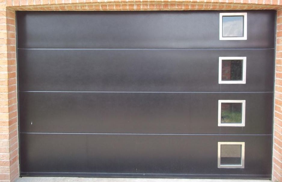 Porte de garage noire avec quatre petites fenêtres carrées, encadrée de briques.