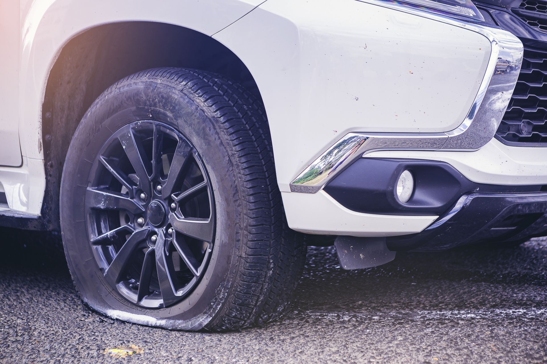 Gros plan sur la roue avant crevée et le pare-chocs d'un SUV blanc sur une route mouillée.