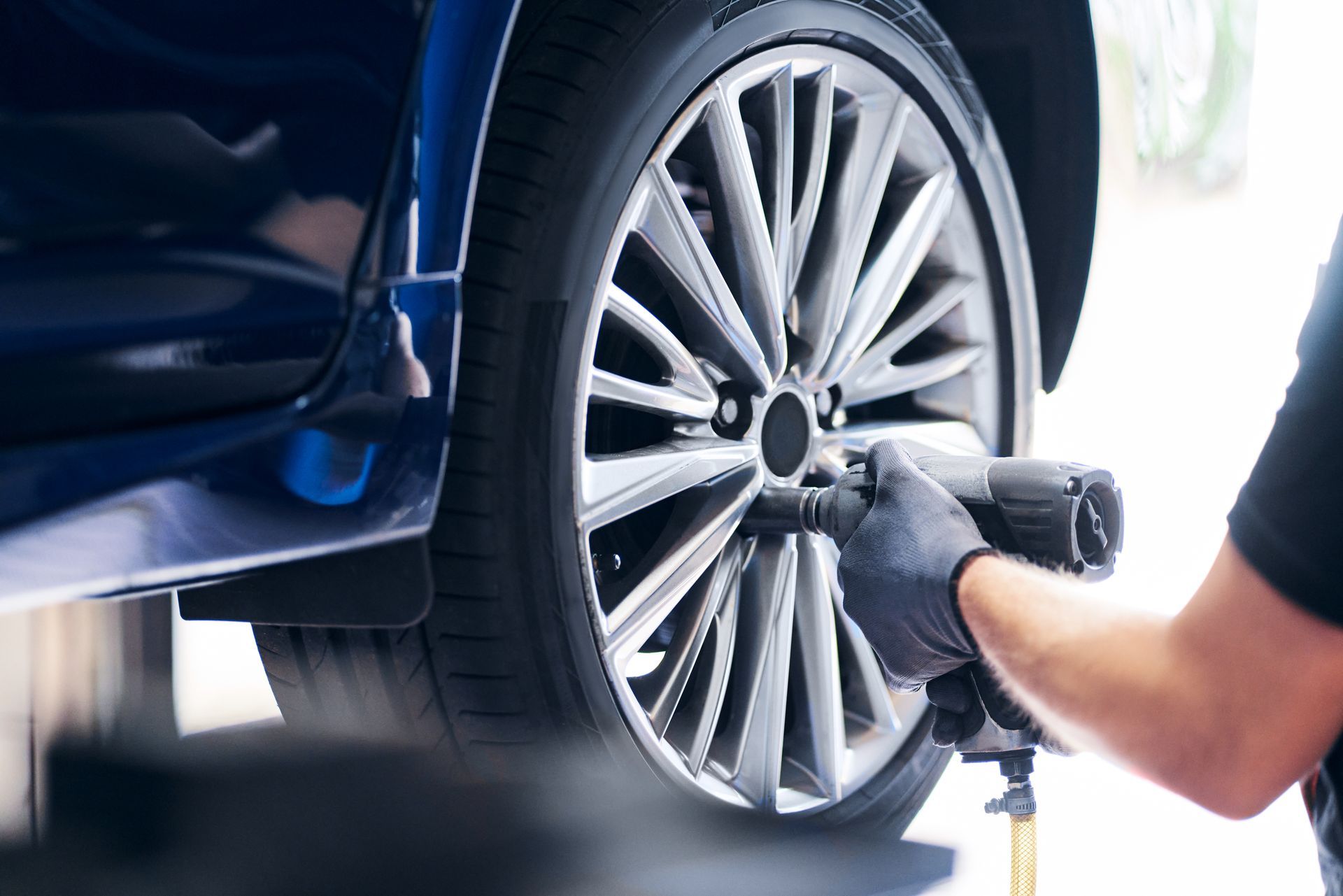 Un mécanicien utilise une clé à choc pour retirer une roue d'une voiture bleue.