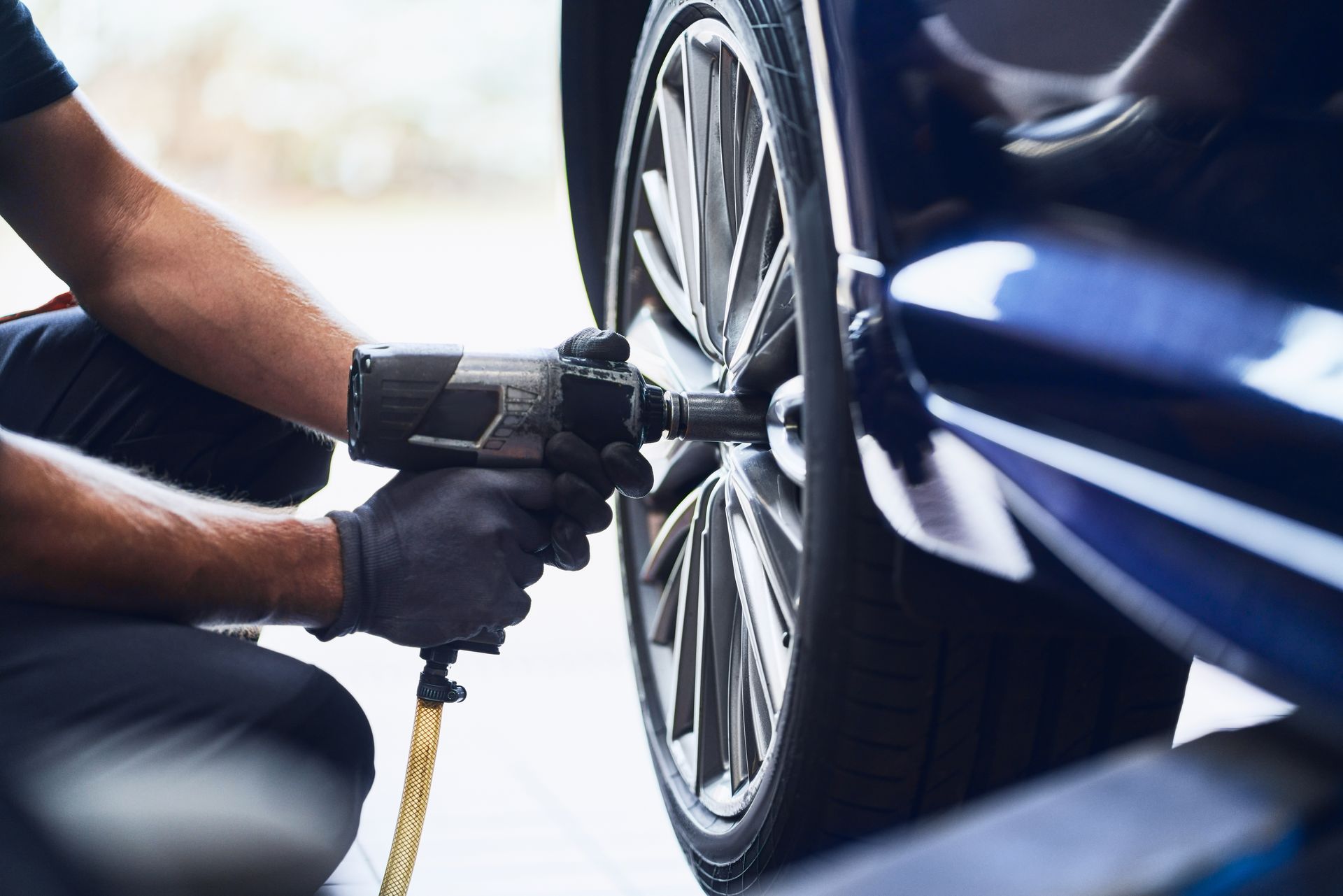 Un mécanicien utilise une clé pneumatique pour serrer une roue de voiture sur un véhicule bleu.
