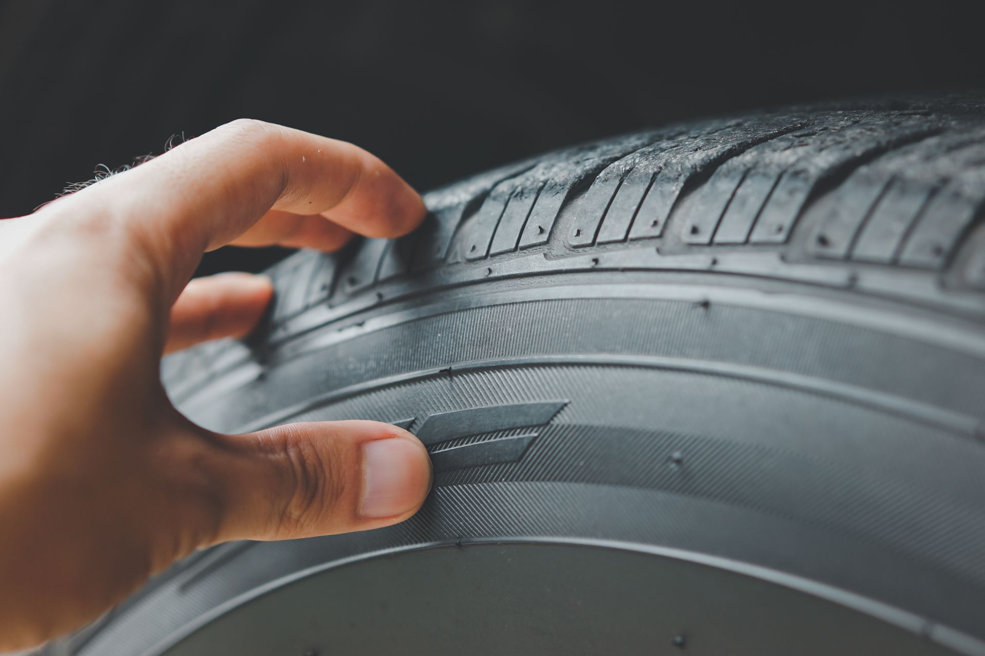 Gros plan d'une main vérifiant la bande de roulement d'un pneu de voiture noir.