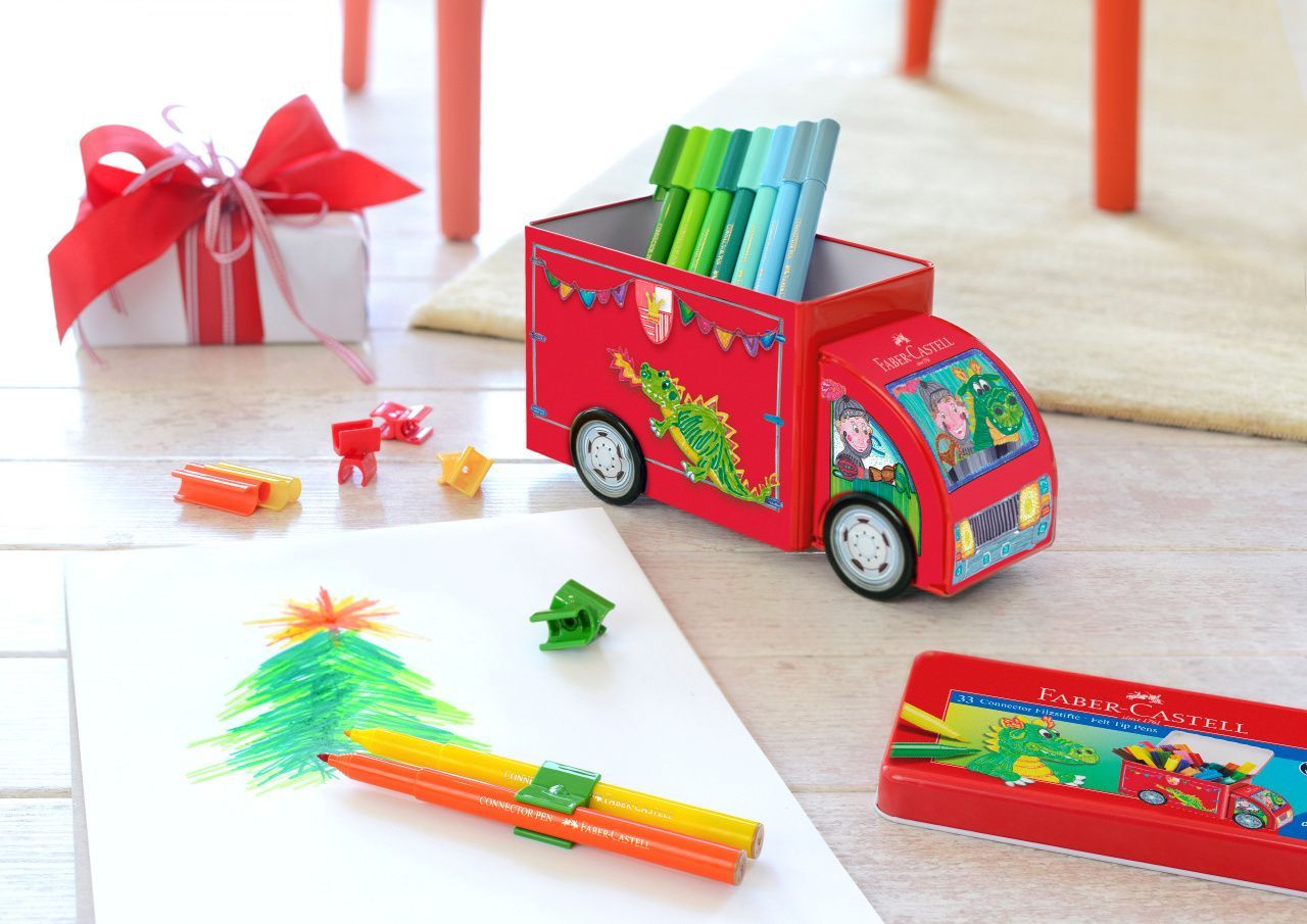 Un organiseur de bureau en forme de camion jouet rouge rempli de feutres, posé sur un sol blanc à côté d'un dessin d'arbre, d'un cadeau et d'une boîte à crayons.