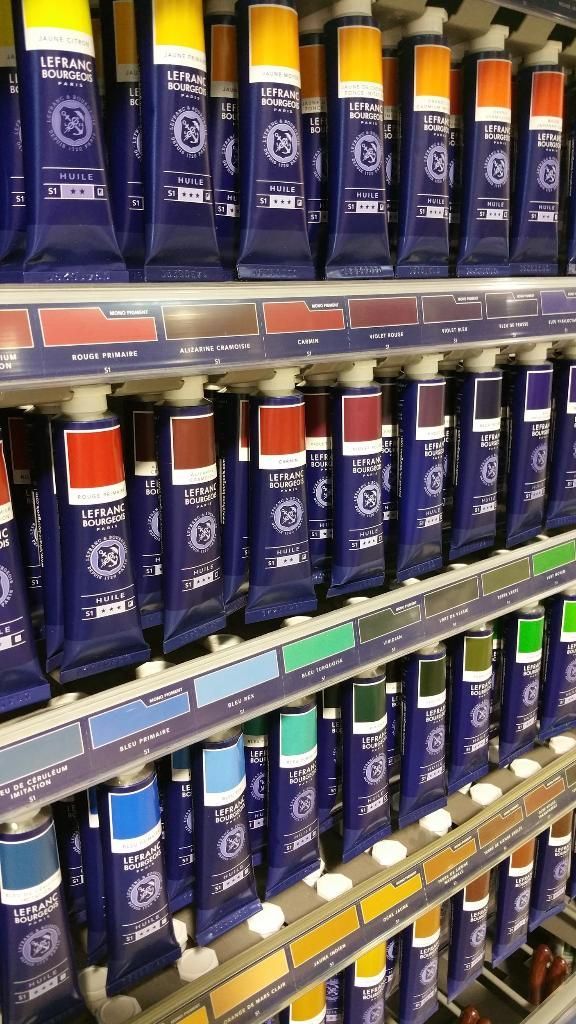 Des tubes de peinture avec des bouchons de différentes couleurs sont présentés sur les étagères d'un magasin.