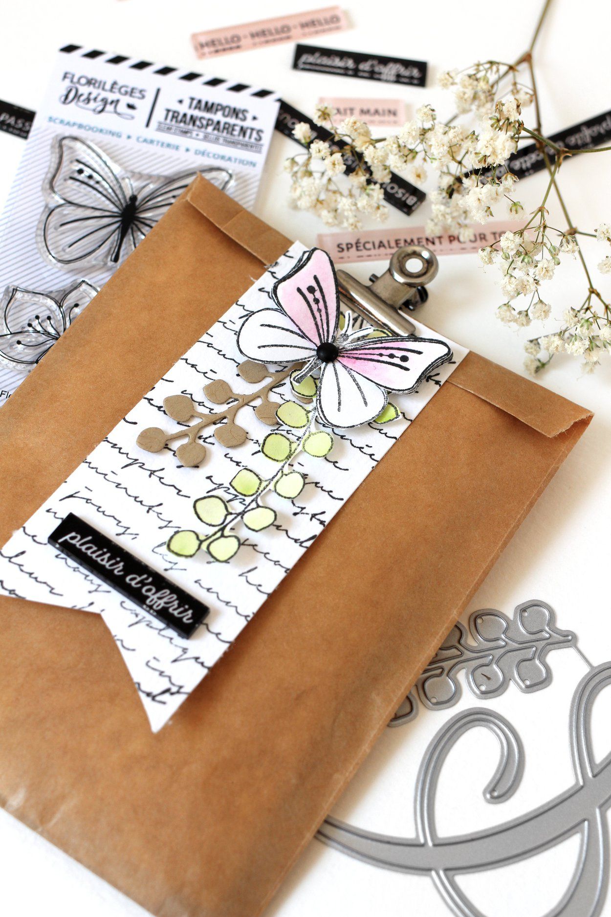 Enveloppe en papier kraft brun avec trombone décoré, timbres et fleurs.