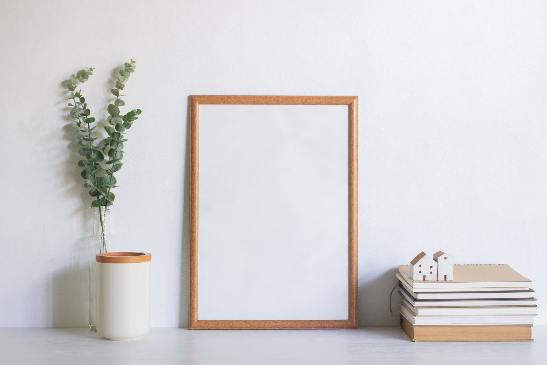 Cadre en bois avec un espace blanc vide, de la verdure, des livres et une petite maison sur une table blanche.