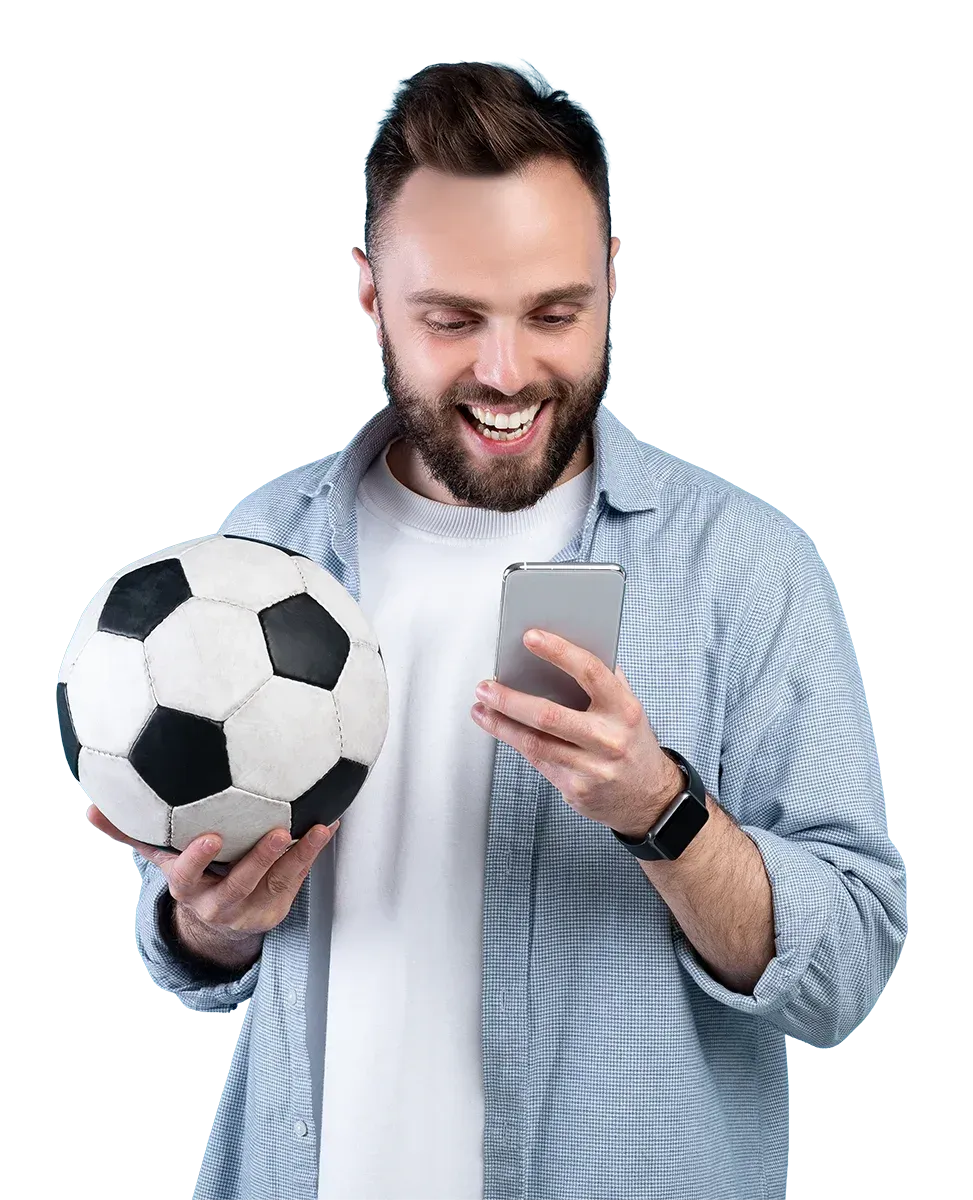 Eine lächelnde Person in einem blauen Hemd hält einen Fußball und schaut auf ein Smartphone.