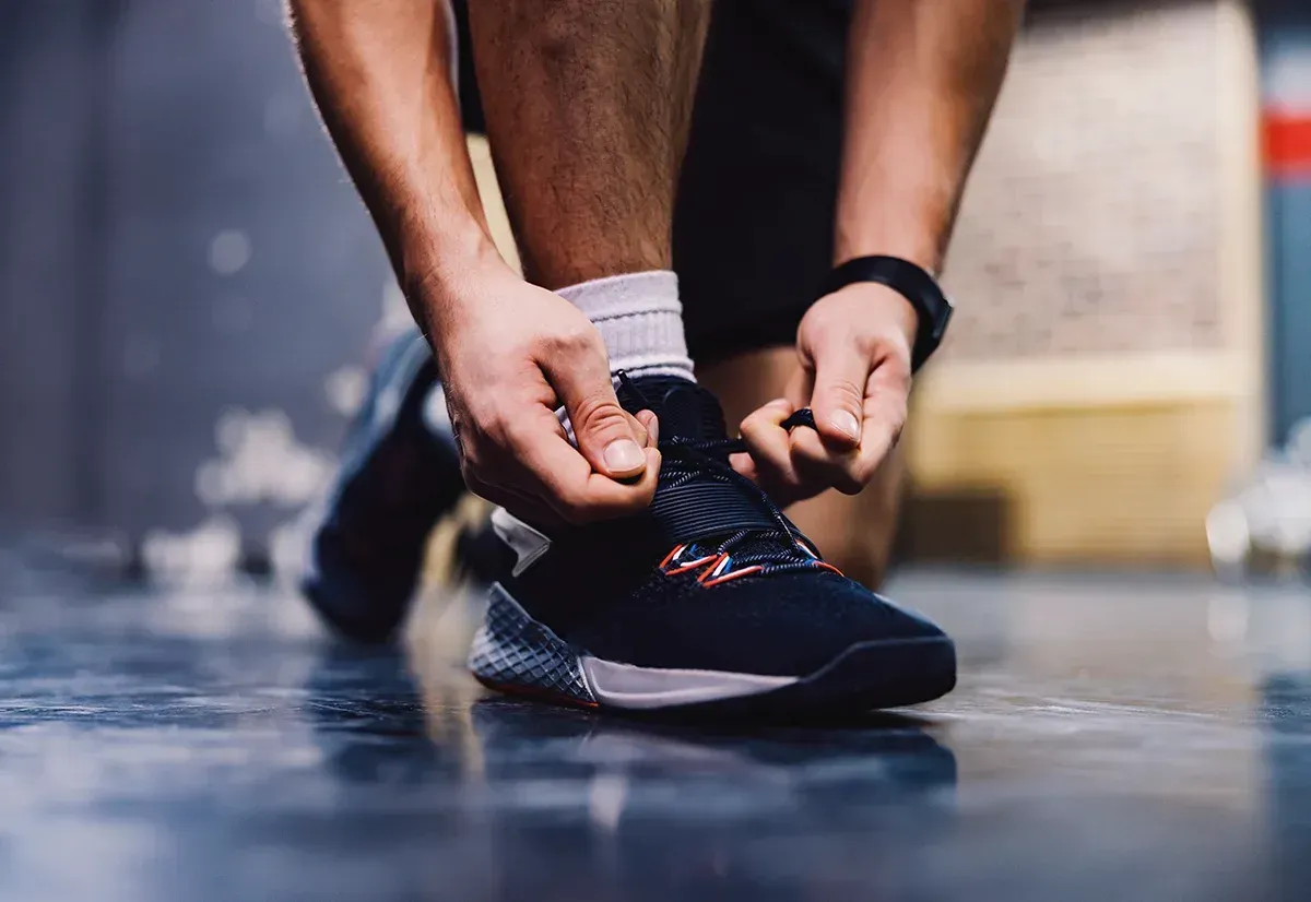Nahaufnahme einer Person, die in einer Turnhalle die Schnürsenkel eines schwarzen Sportschuhs bindet.