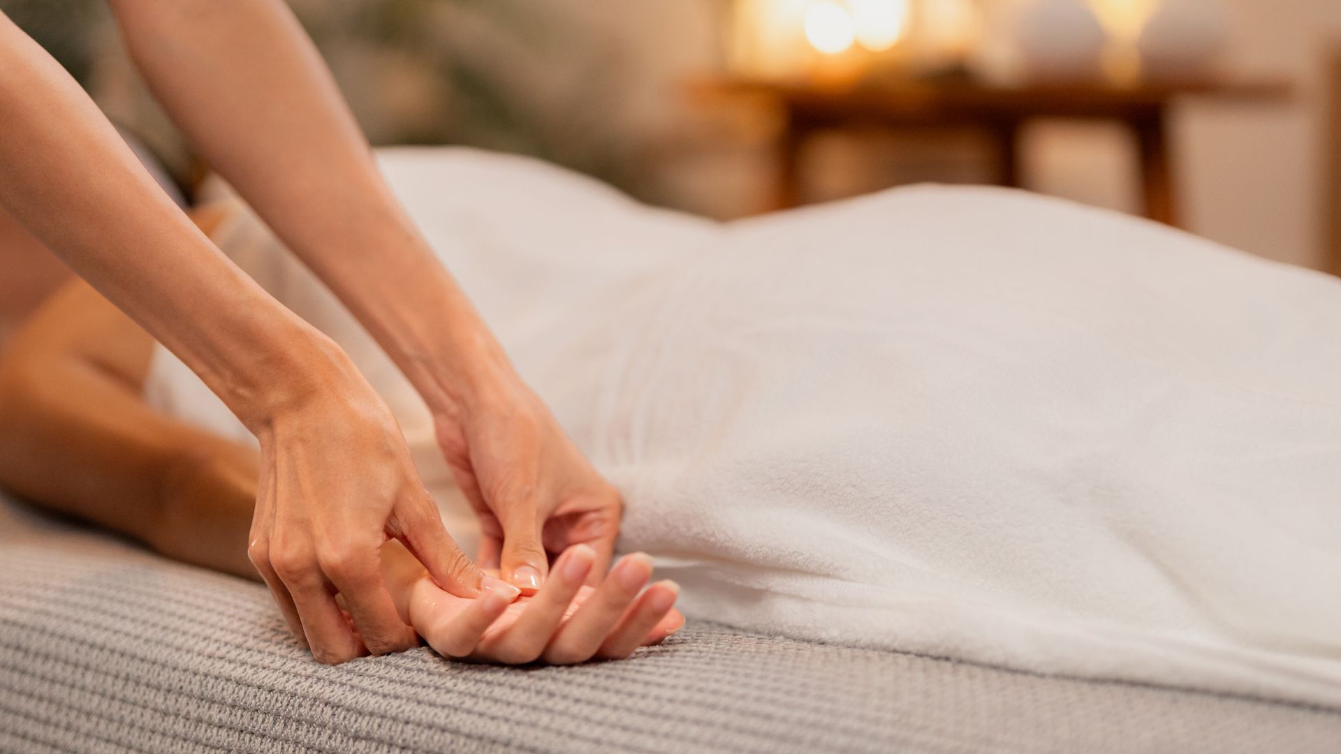 Des mains massent la main d'une personne allongée sur une table de massage recouverte d'une serviette blanche.