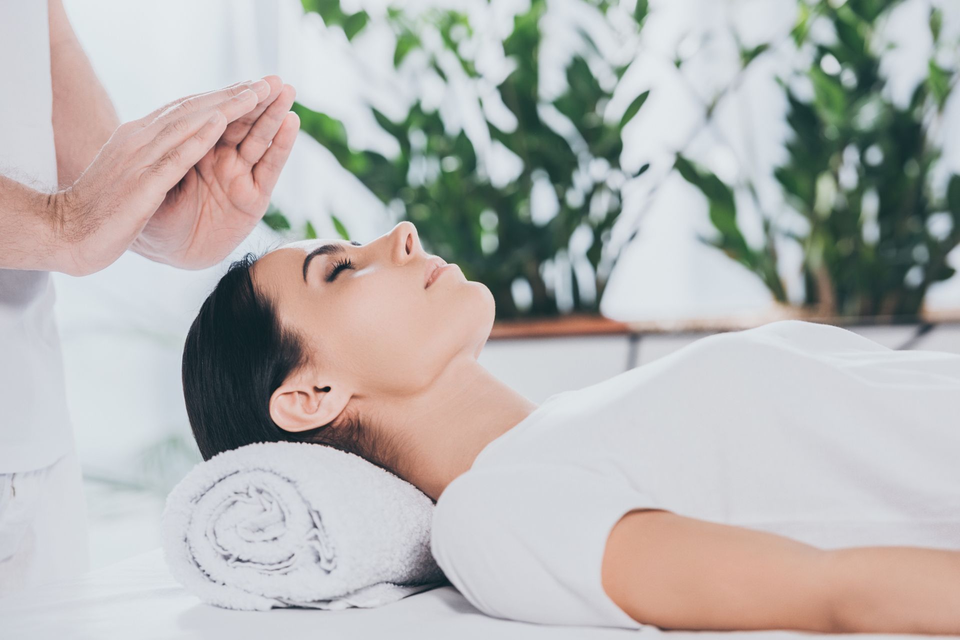 Femme recevant un soin reiki, mains au-dessus de sa tête, pièce blanche.