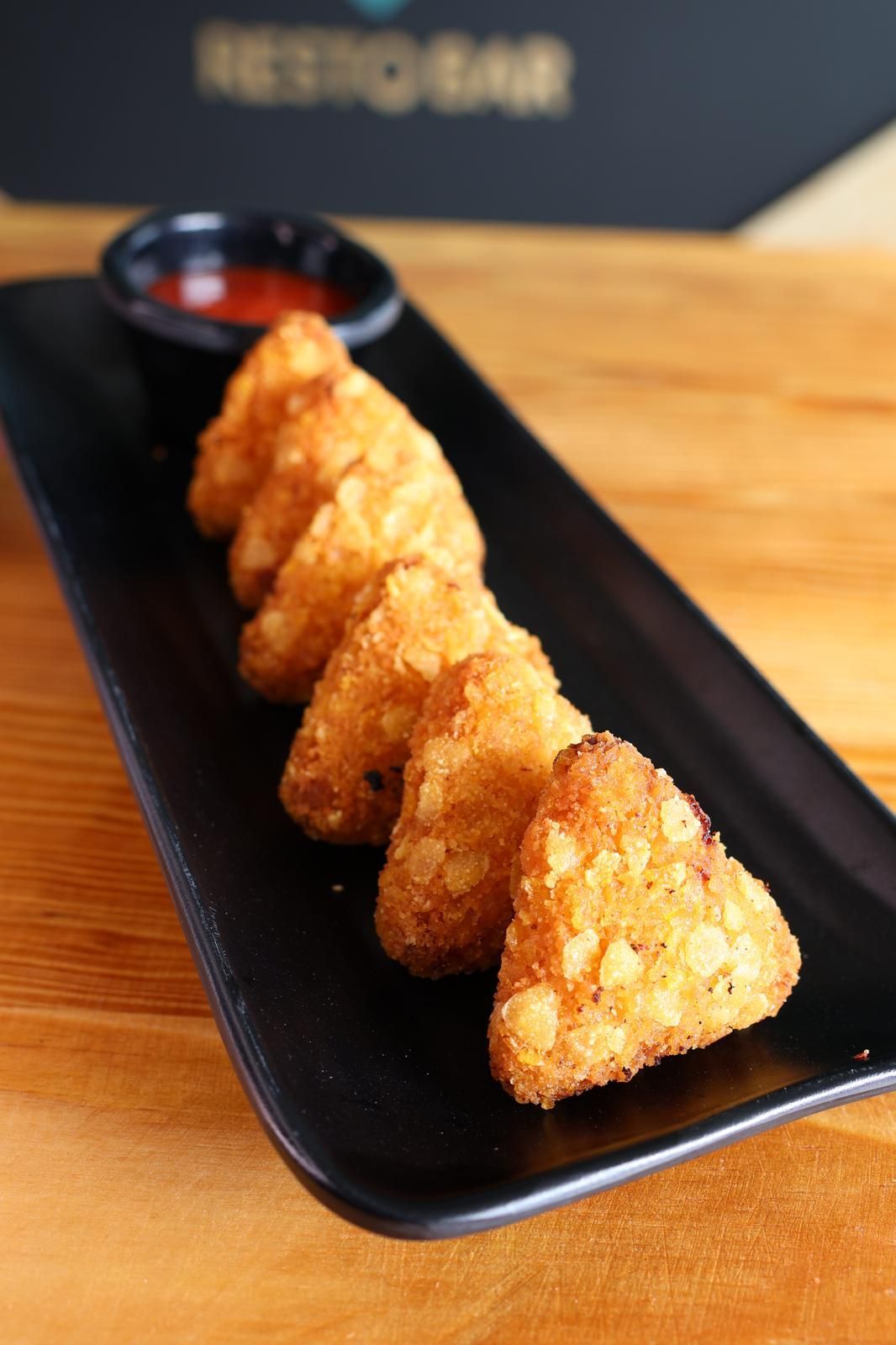 Comida frita en un plato negro con salsa para mojar