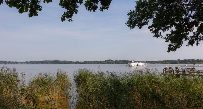 Ein Boot schwimmt auf einem See, im Vordergrund sind Bäume zu sehen.